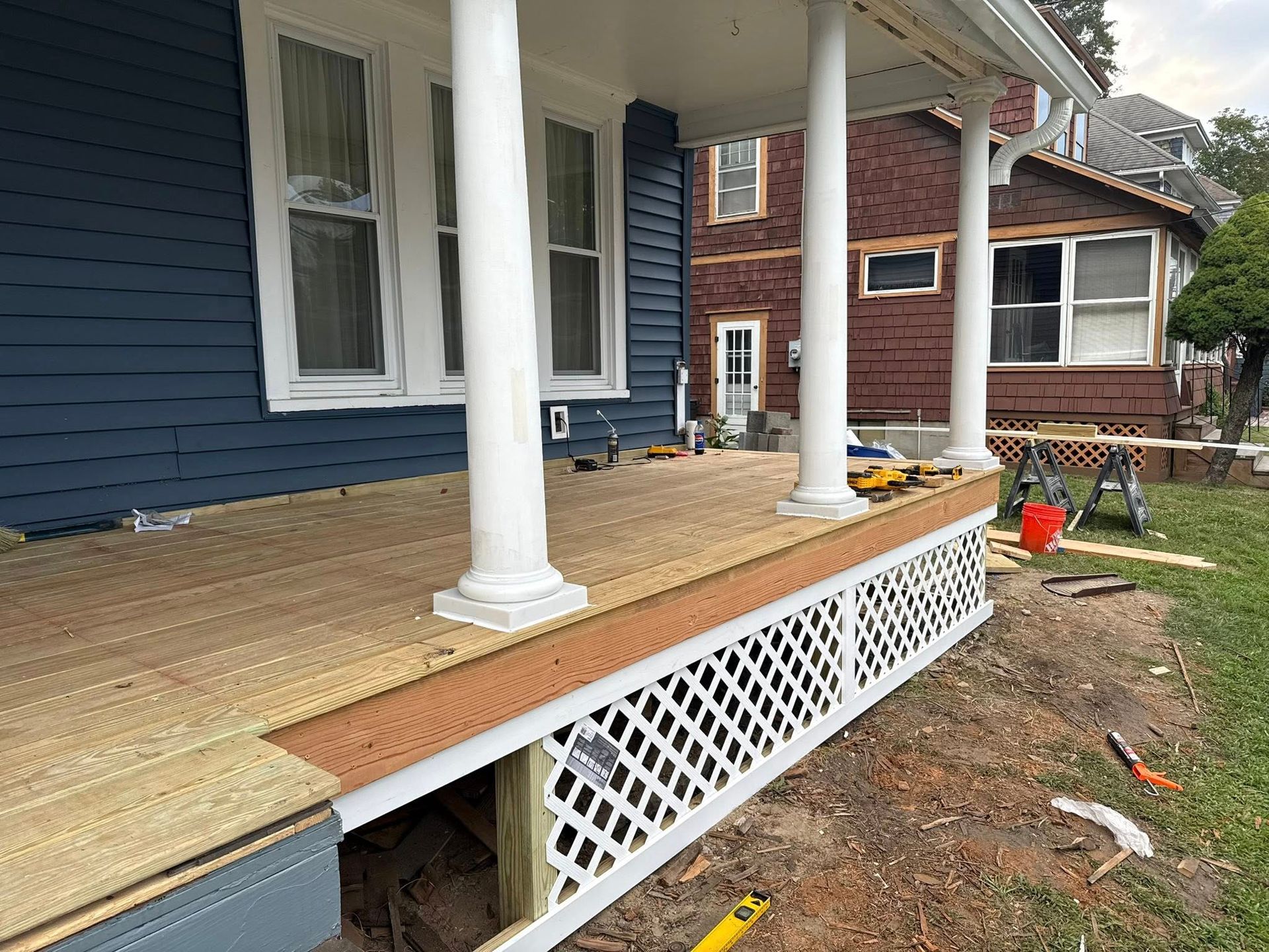 A house porch under construction with new deck boards and lattice skirting.