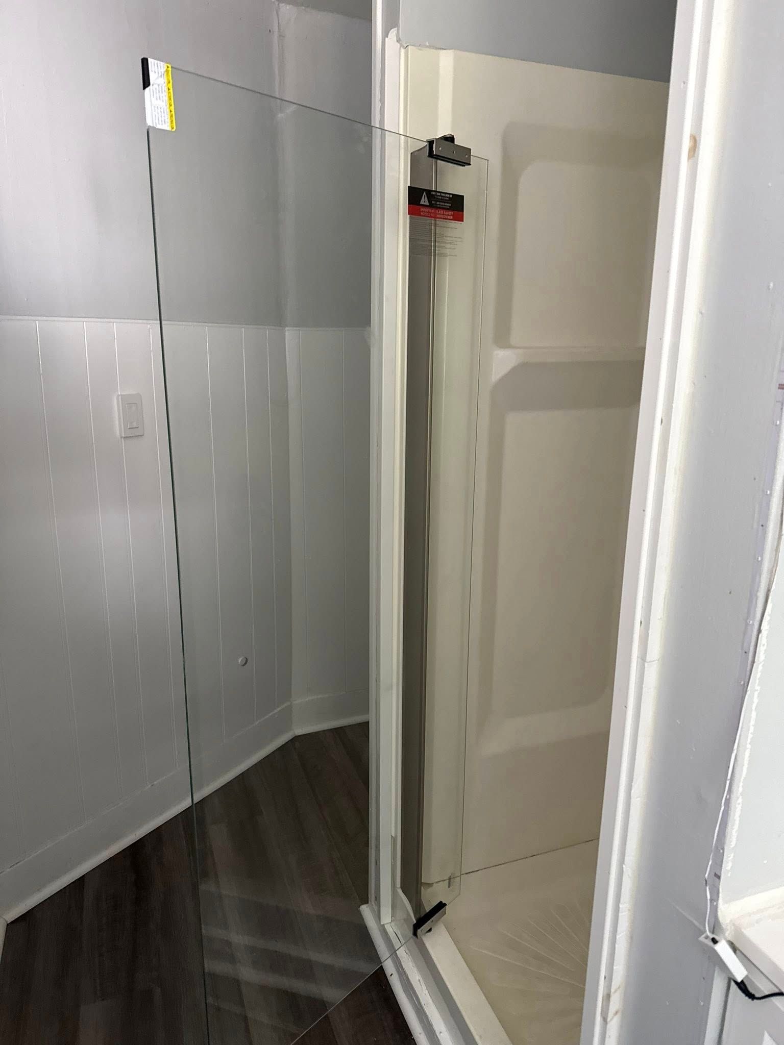 Shower with clear glass door, white enclosure, and dark wood-look floor.