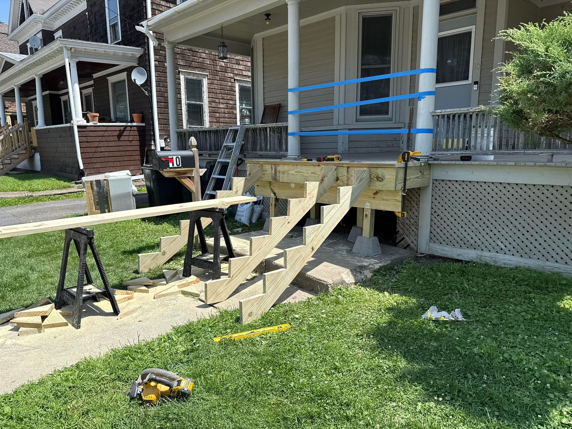 A house with wooden stairs under construction. Blue tape and sawhorses are present. Green grass and sidewalk.