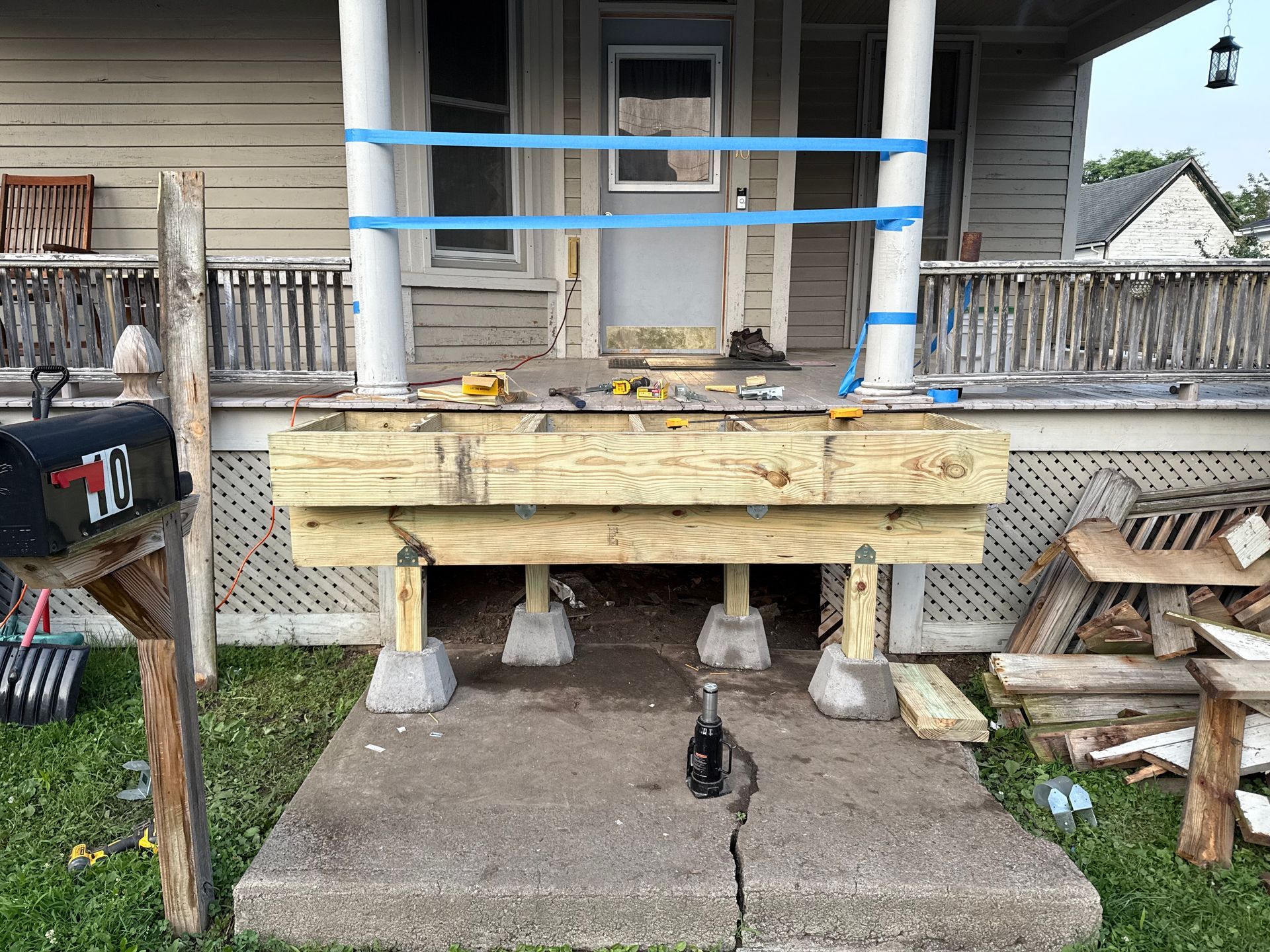 Porch under construction; new wooden deck supported by concrete blocks, with blue tape on porch columns.