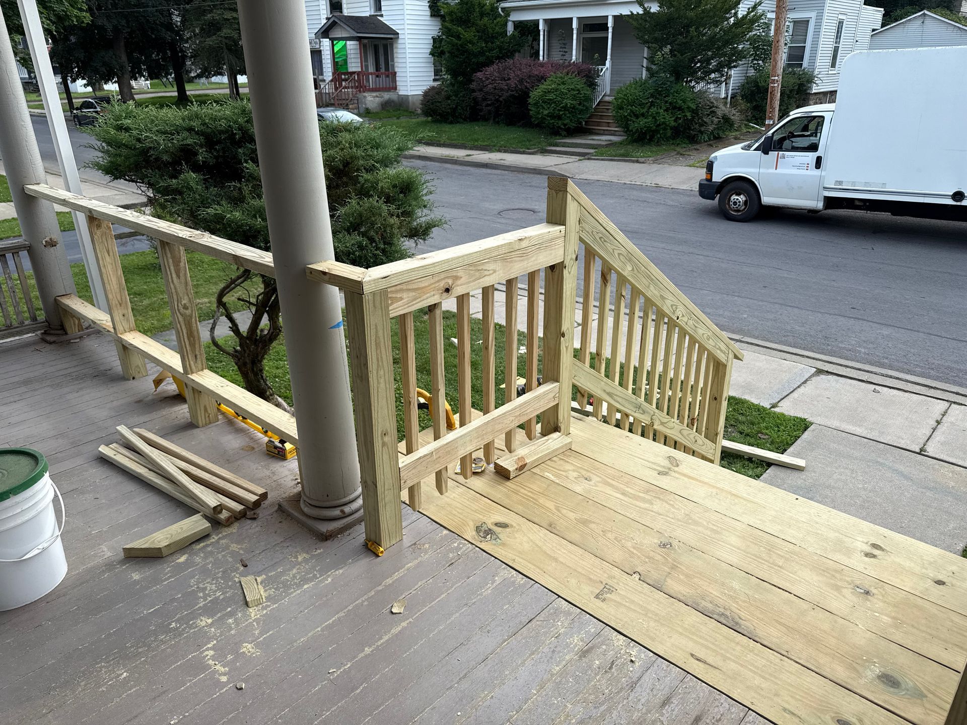 A wooden porch with steps and railing under construction, a white van parked on the street.