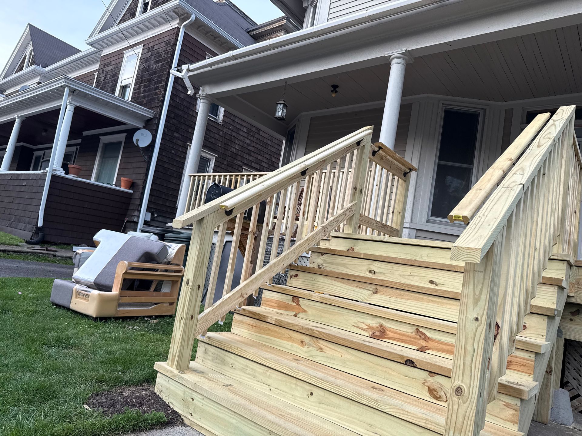 Wooden stairs and railing leading up to a porch with a gray house in the background.