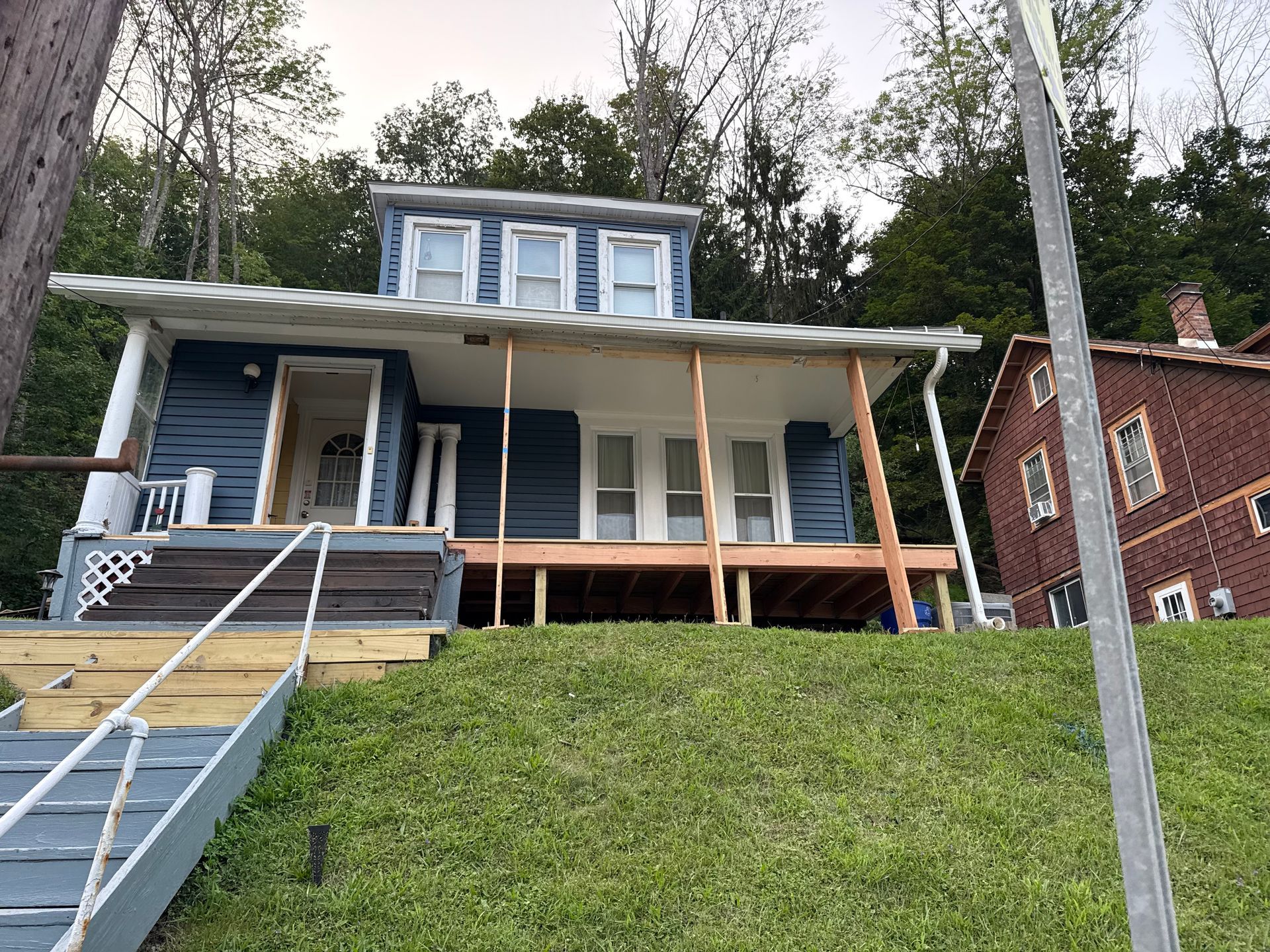 Blue house with porch on a grassy hill; wooden stairs lead up to the porch.