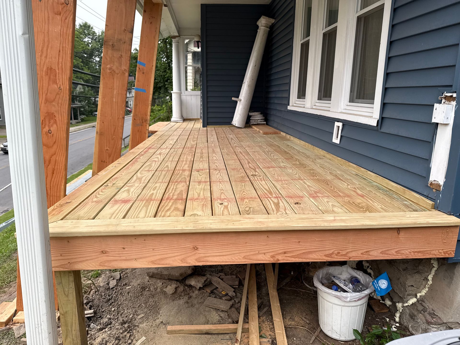Newly built wooden deck attached to a blue house with exposed support beams.