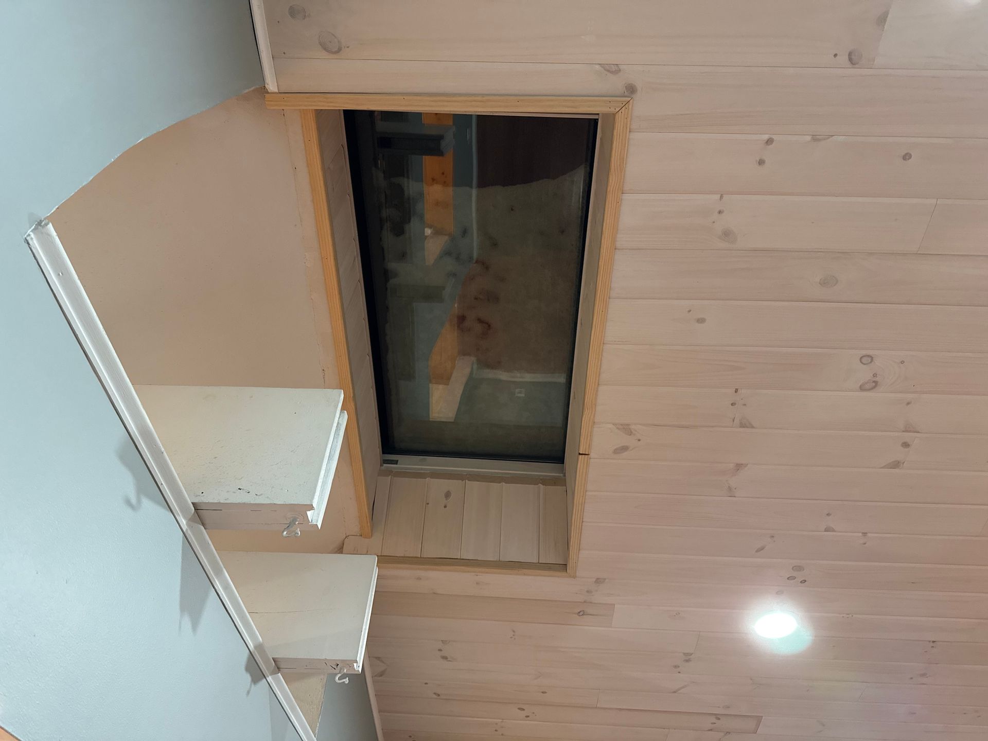 Interior view: a skylight in a light wood paneled ceiling, steps leading up a wall painted blue.