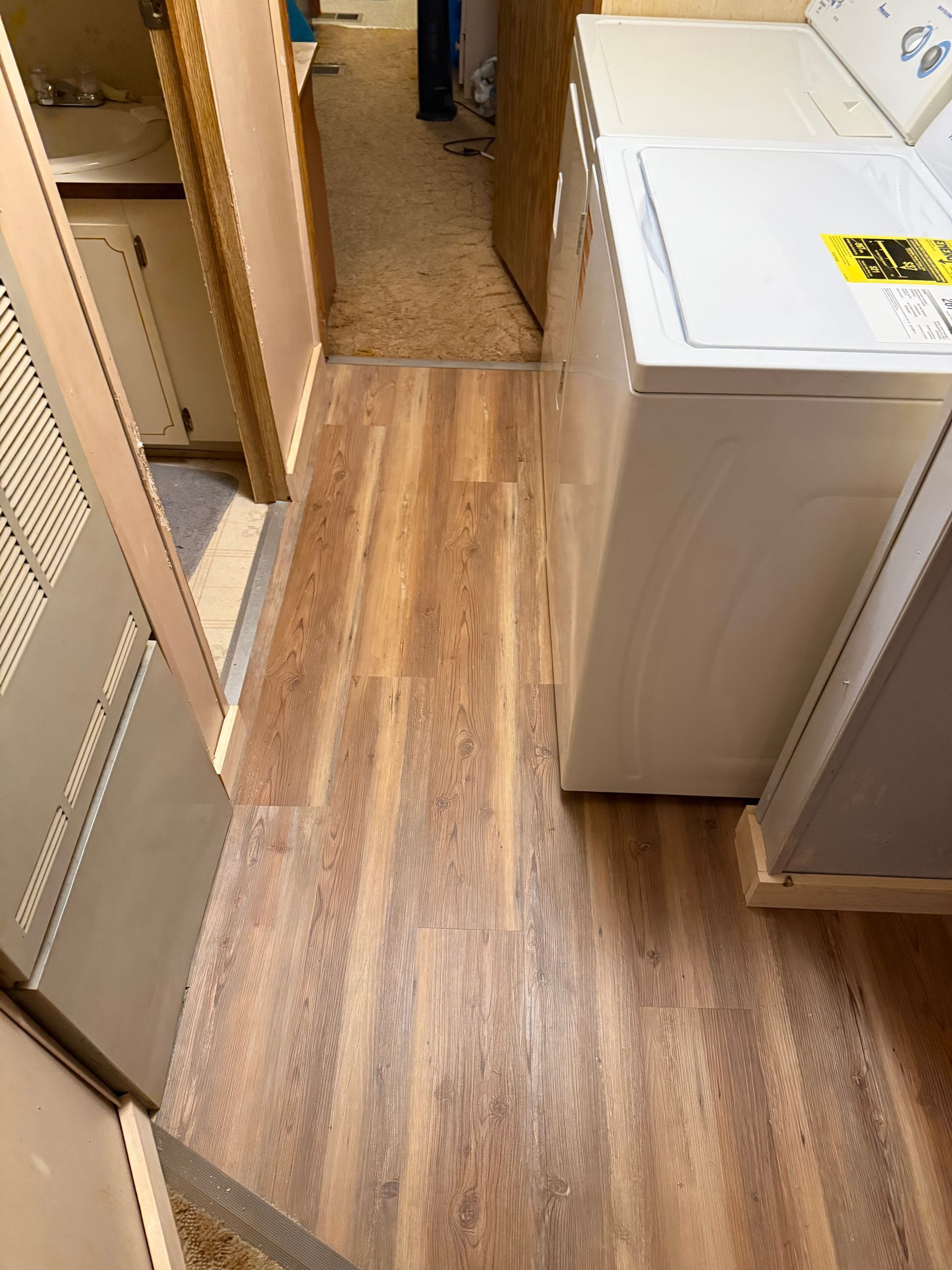 Wooden-look flooring in a narrow hallway with a washing machine and door on either side.