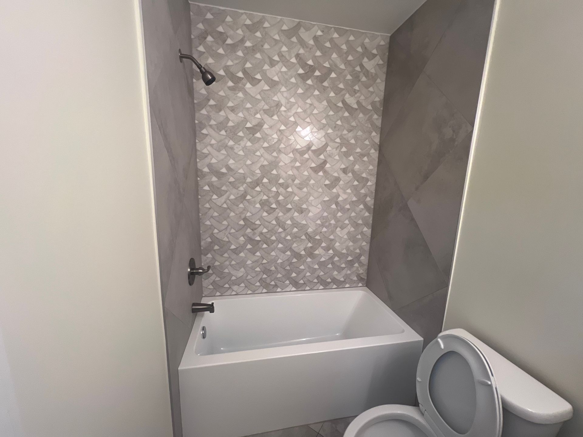 Bathroom with white bathtub, gray tile shower surround, and white toilet.