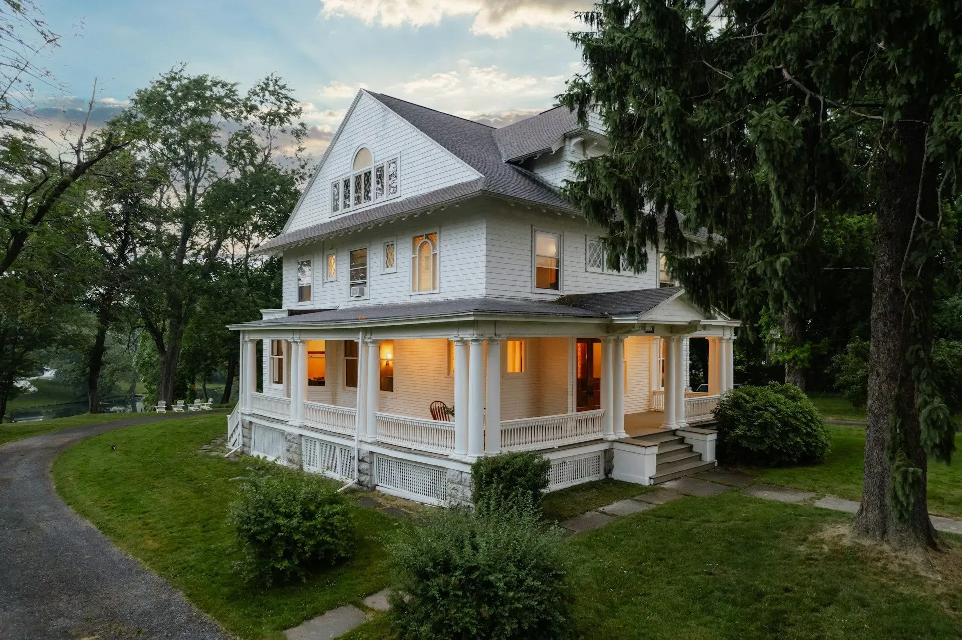 A large white house with a large porch is surrounded by trees.