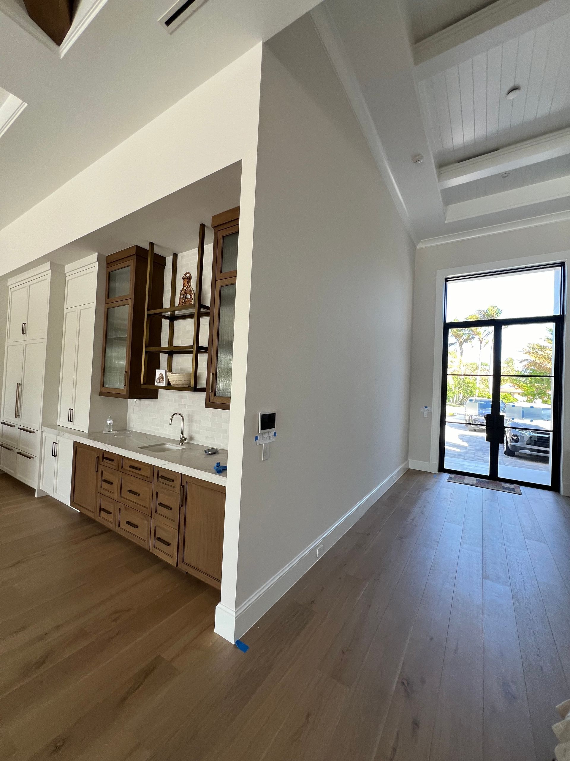 Interior view with a kitchen, cabinets, and a doorway to the outside. Wooden floors and light walls.