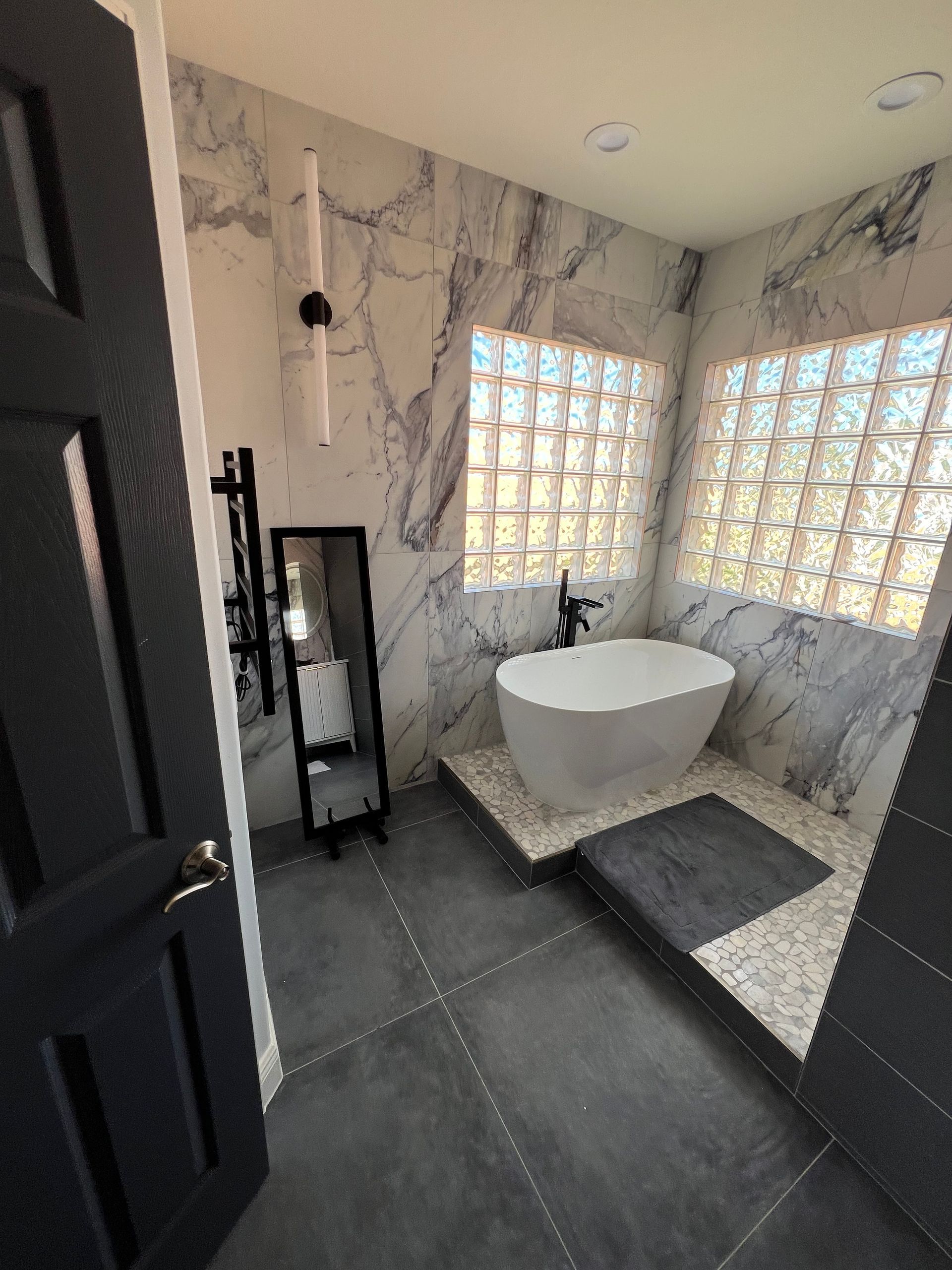 Modern bathroom with a white soaking tub, marble walls, and glass block windows.