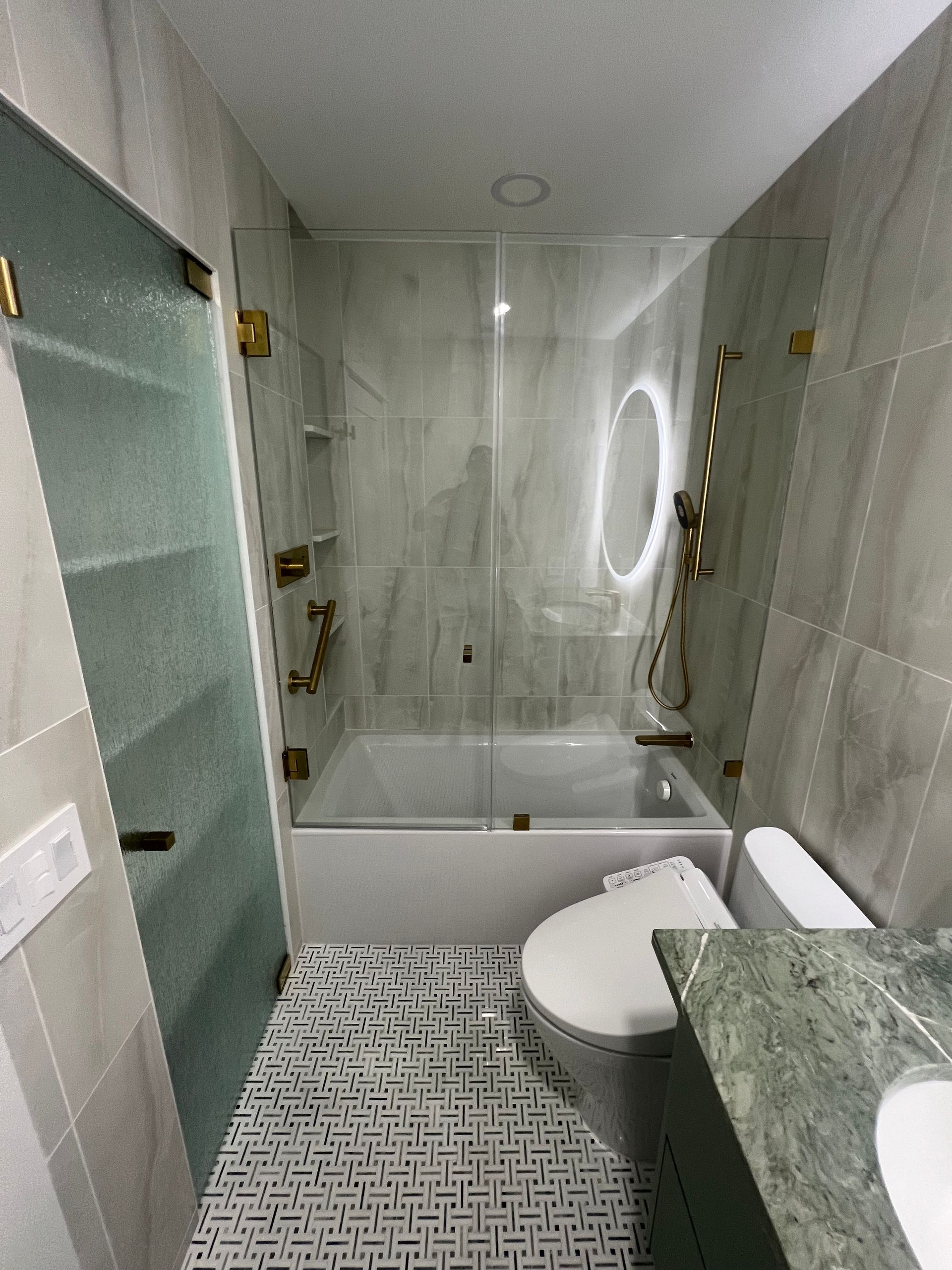 Modern bathroom with white tub, gold fixtures, and patterned tile floor.
