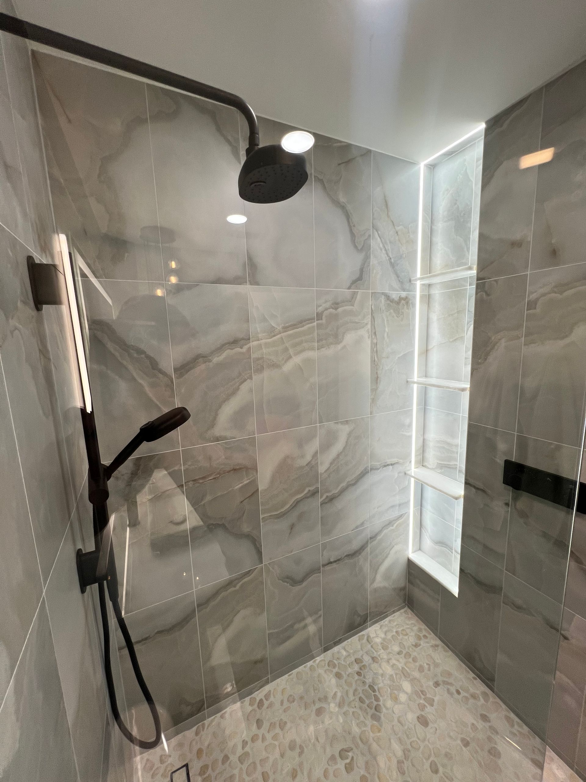 Gray-tiled shower with black fixtures. Glass door on the left, window on the right.