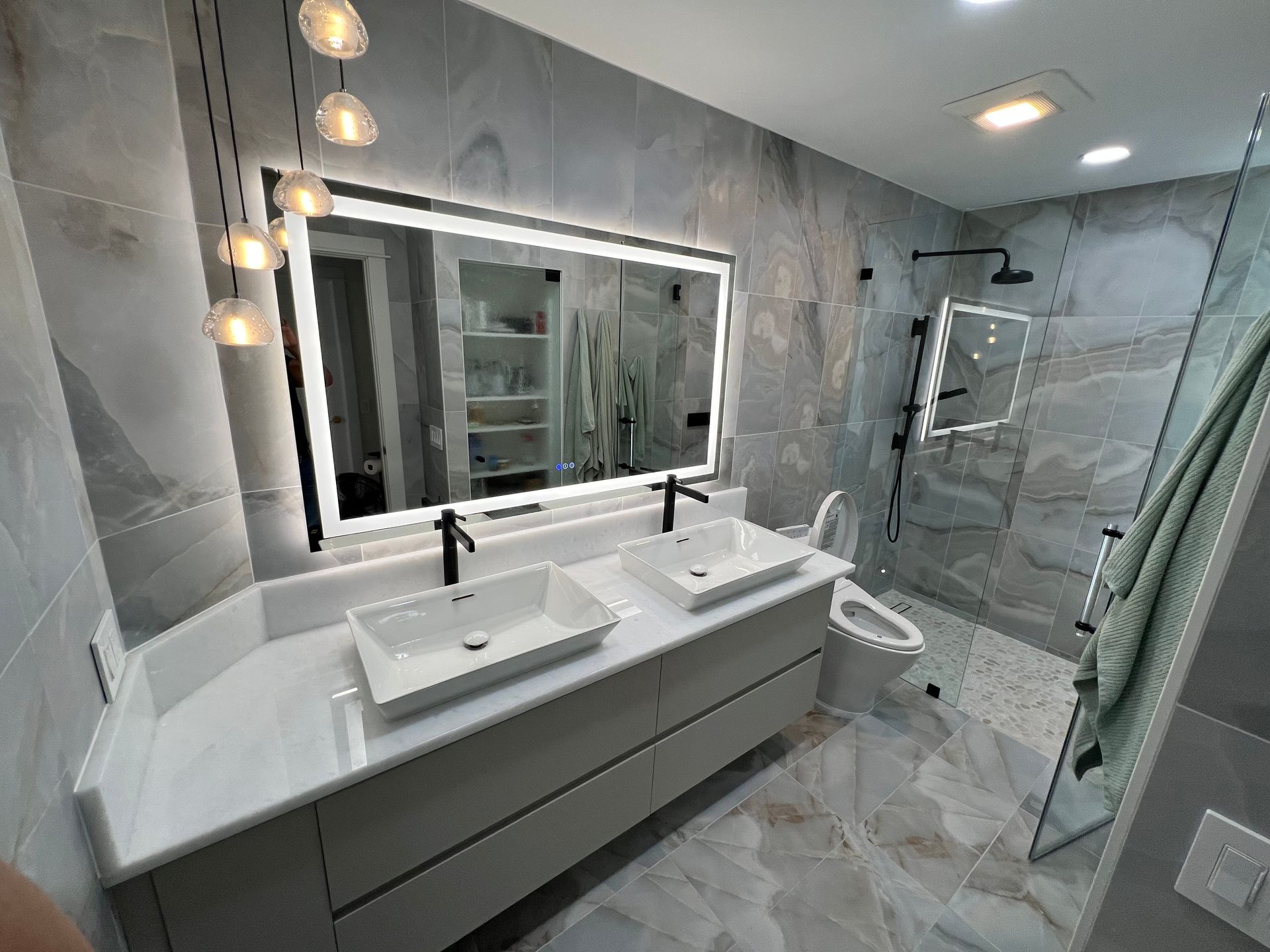 Modern bathroom with gray tile, a double vanity, and a large mirror with lights.