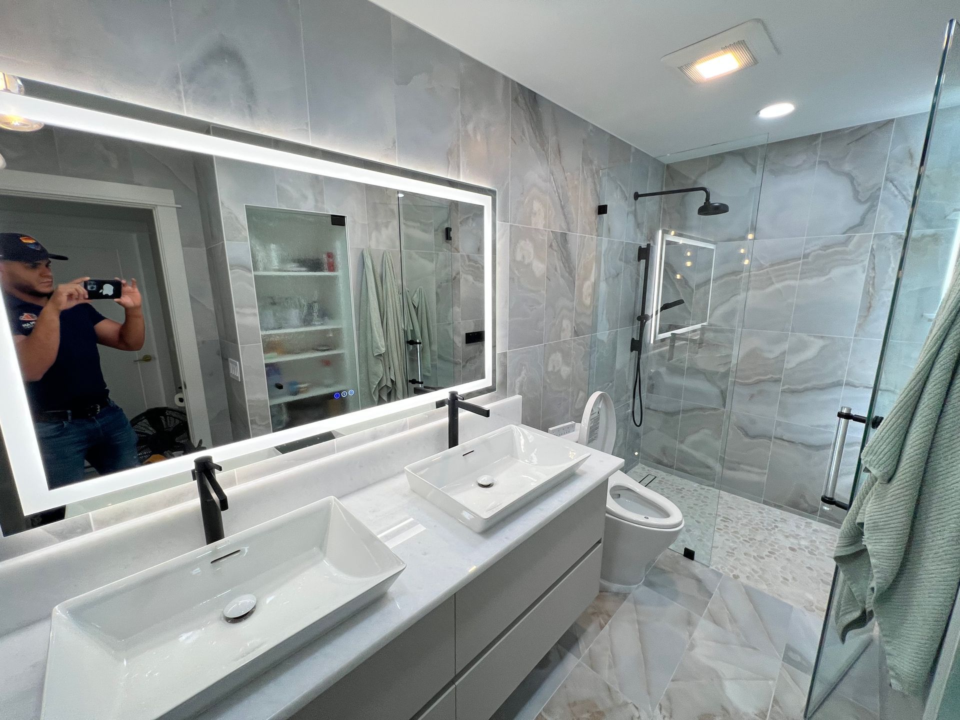 Modern bathroom with double sinks, large mirror, tiled walls, glass shower.