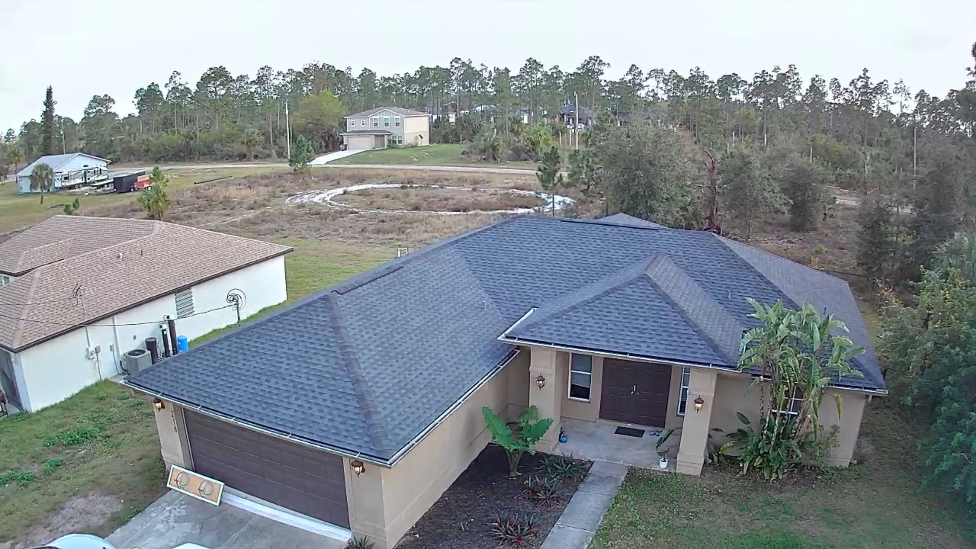 A modern, single-story house with a dark roof, set in a rural area with trees.