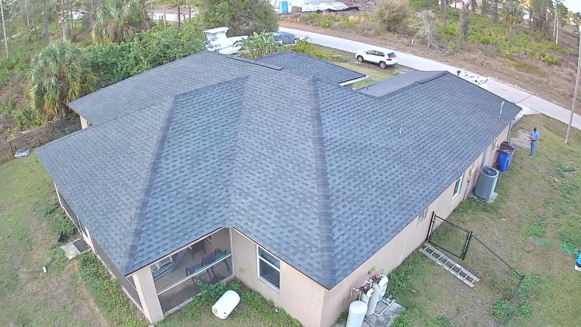 Overhead view of a house with dark gray roof, surrounded by green grass and a nearby road.