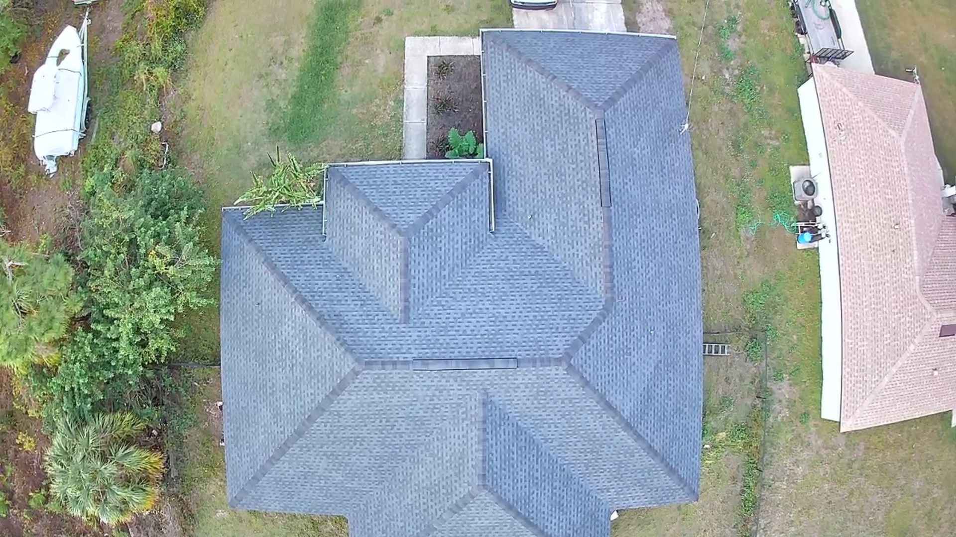 Overhead view of a gray-roofed house with multiple angles, surrounded by grass and a boat on the left.