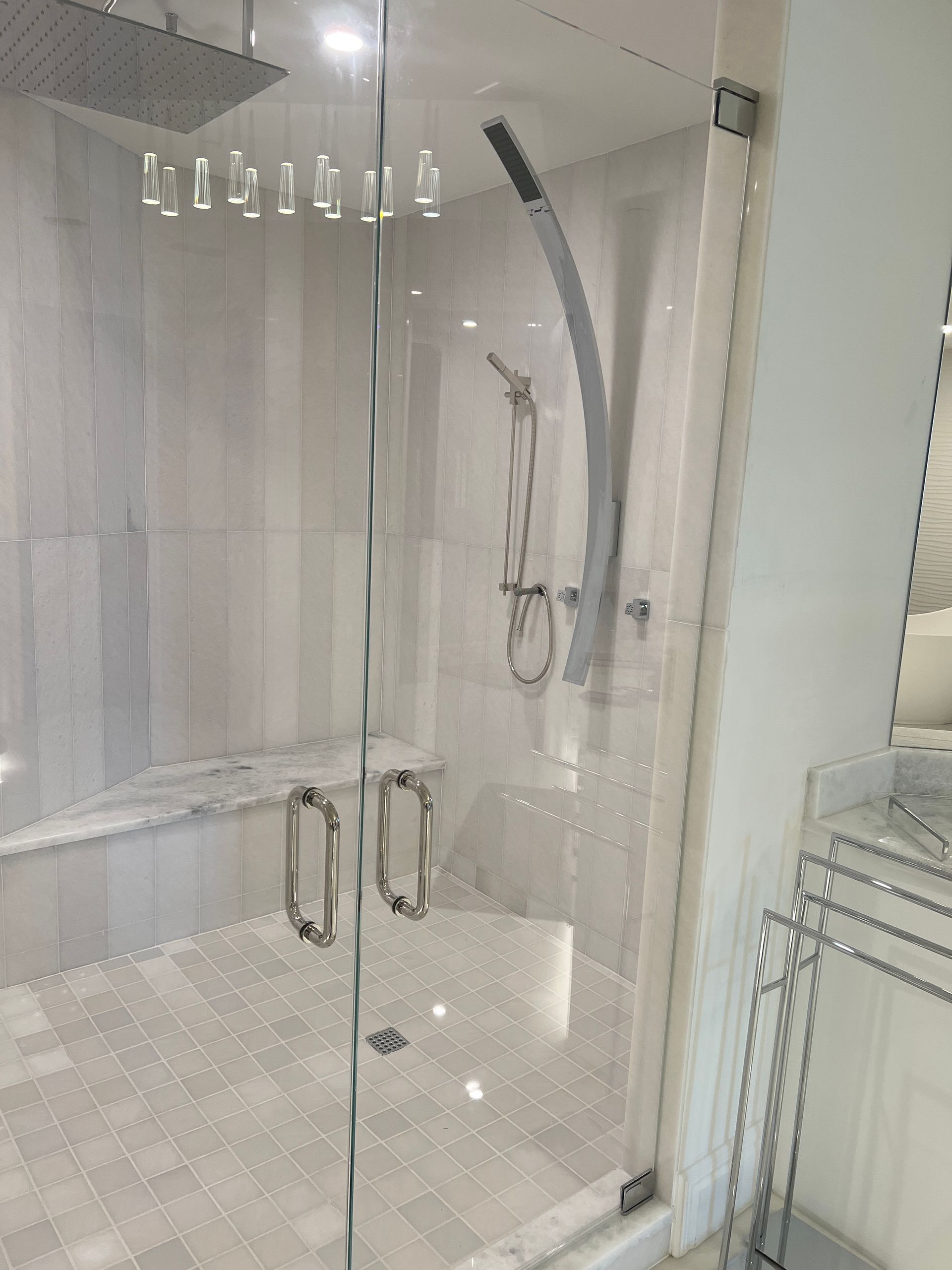 Modern glass shower with white tiled walls, bench, and chrome fixtures.