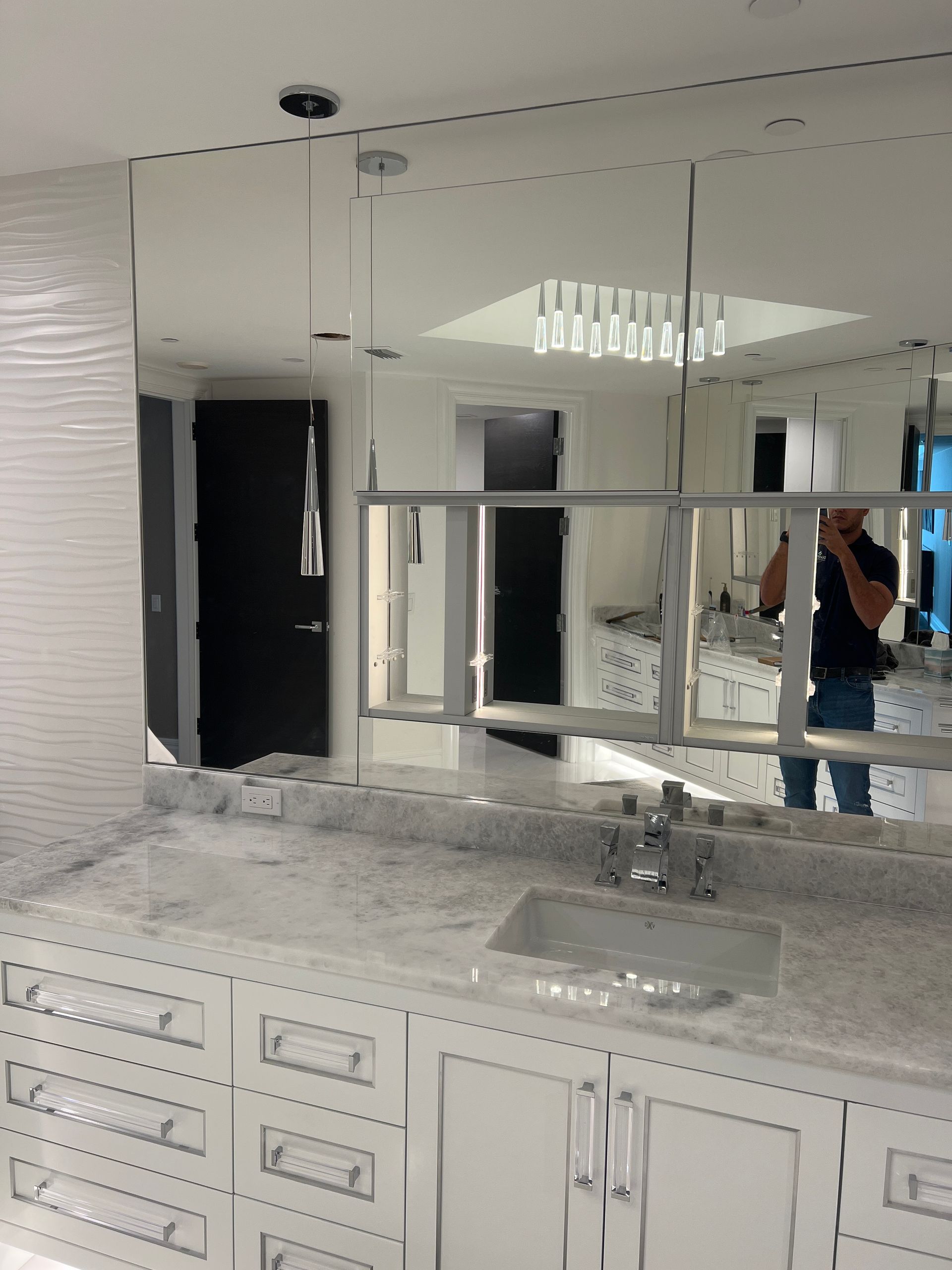 Bathroom with large mirror over a vanity, person reflected in mirror, white cabinets and countertops.