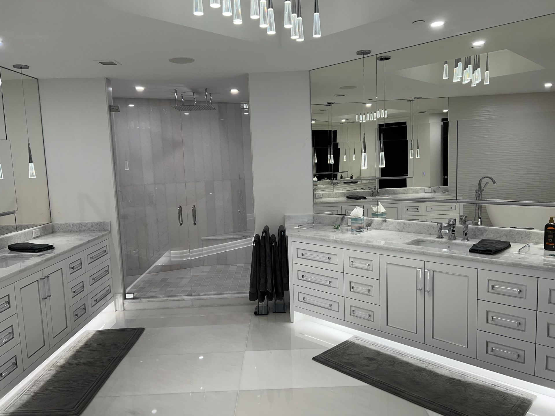 Luxurious modern bathroom with white vanities, large mirrors, and a glass shower.