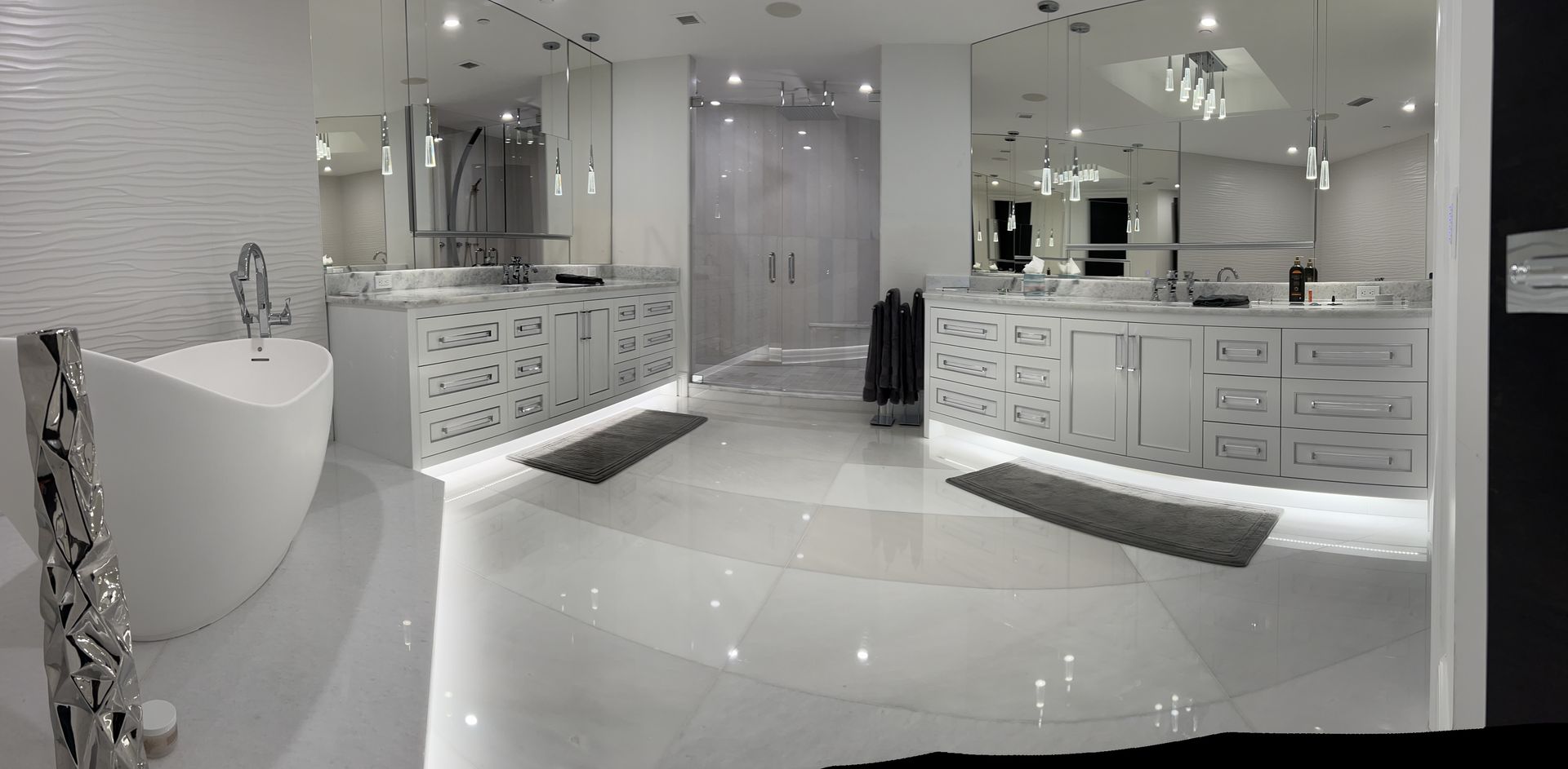 Modern, all-white bathroom. A freestanding bathtub and double sinks on either side, with mirrors and bright lights.