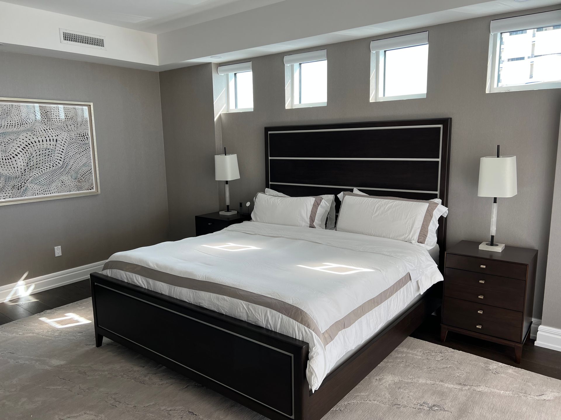 Bedroom with dark wood bed, white bedding, bedside lamps, and three small windows.