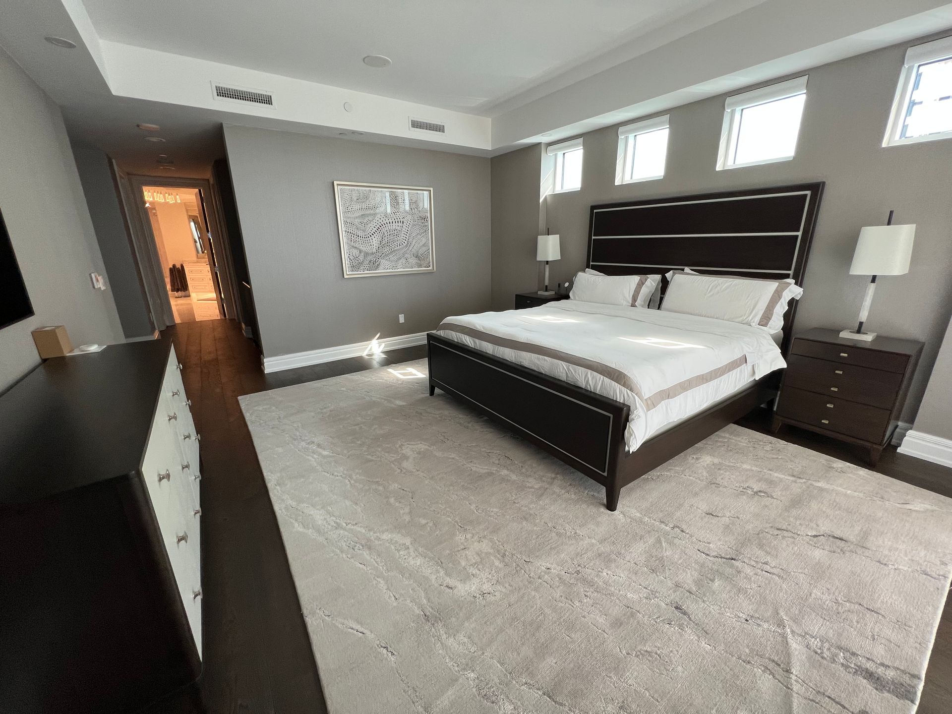 Bedroom with a bed, nightstands, and a large rug. The walls are gray, with white framed windows.