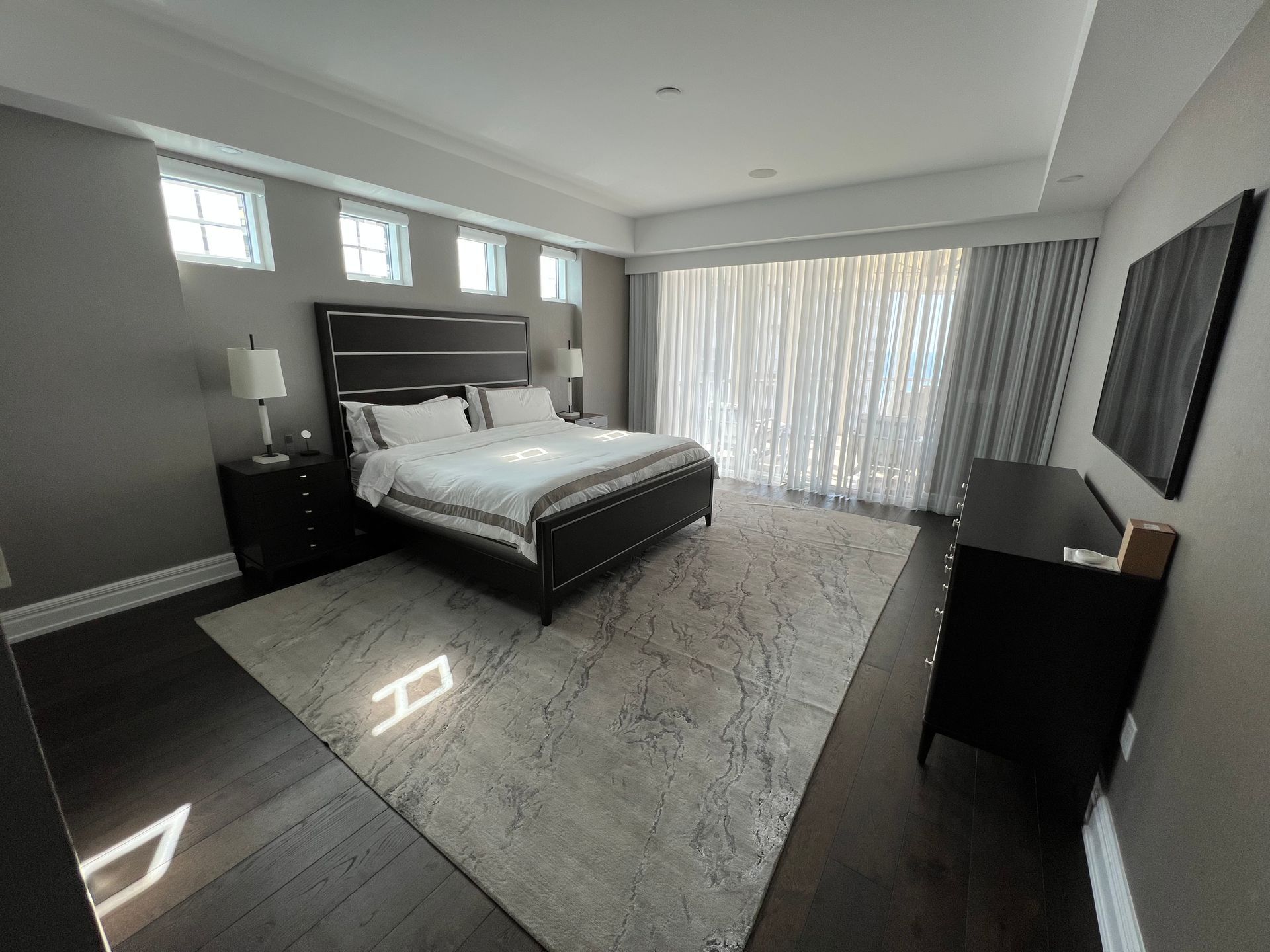 Bedroom with dark furniture, gray walls, large rug, and sheer curtains.