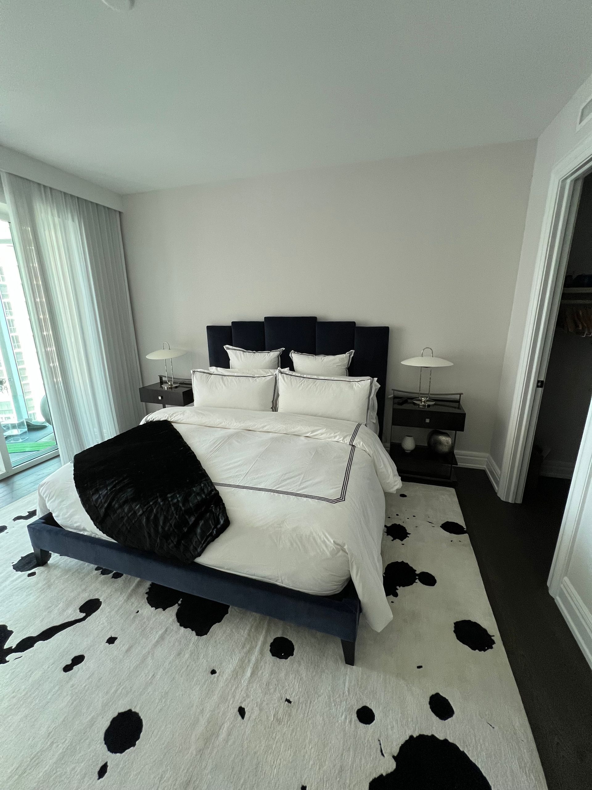 Bedroom with blue bed, white bedding, black throw, and spotted rug.