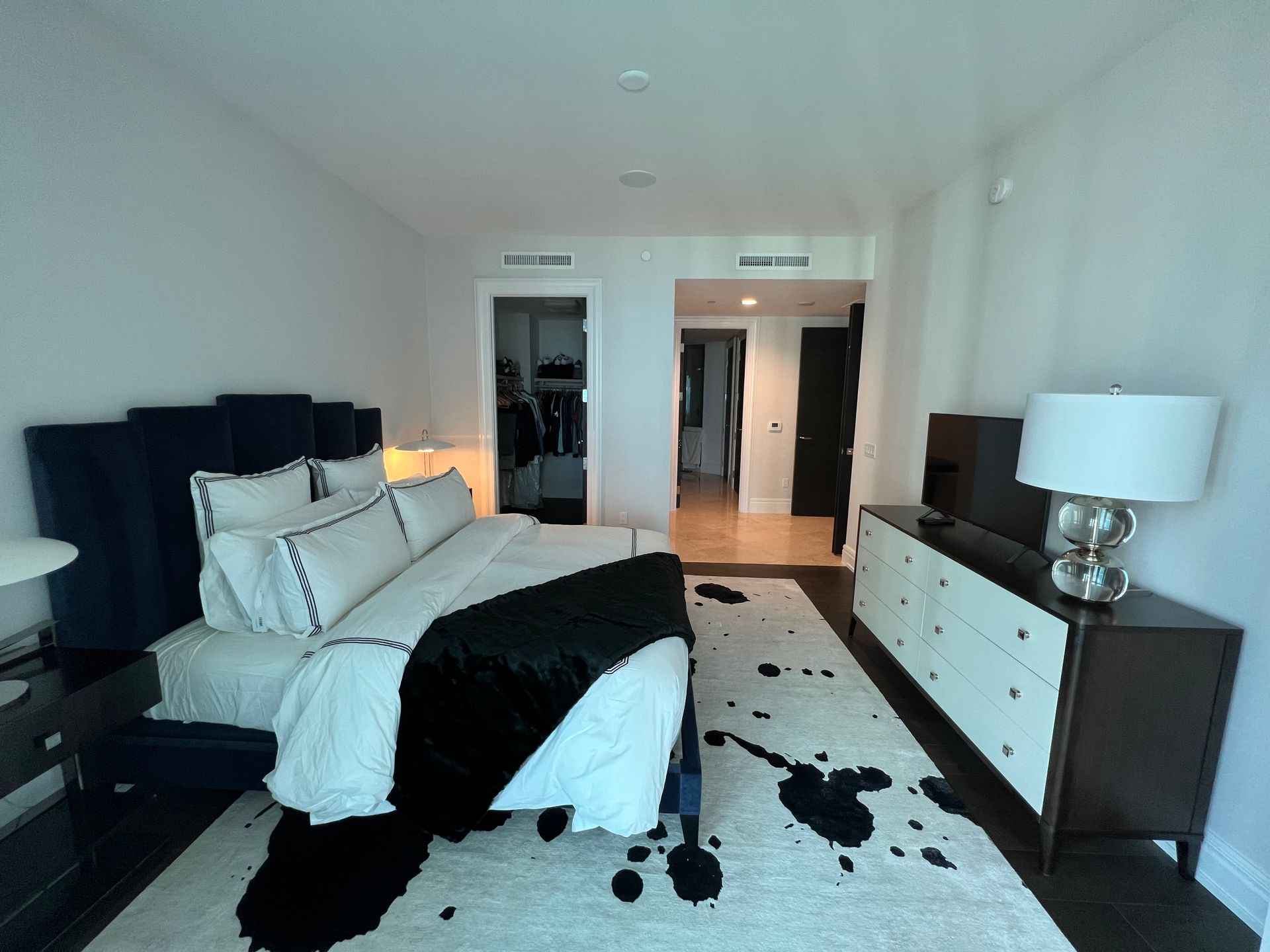 Bedroom with dark blue bed, white bedding, black throw, dresser, black and white rug, and closet.
