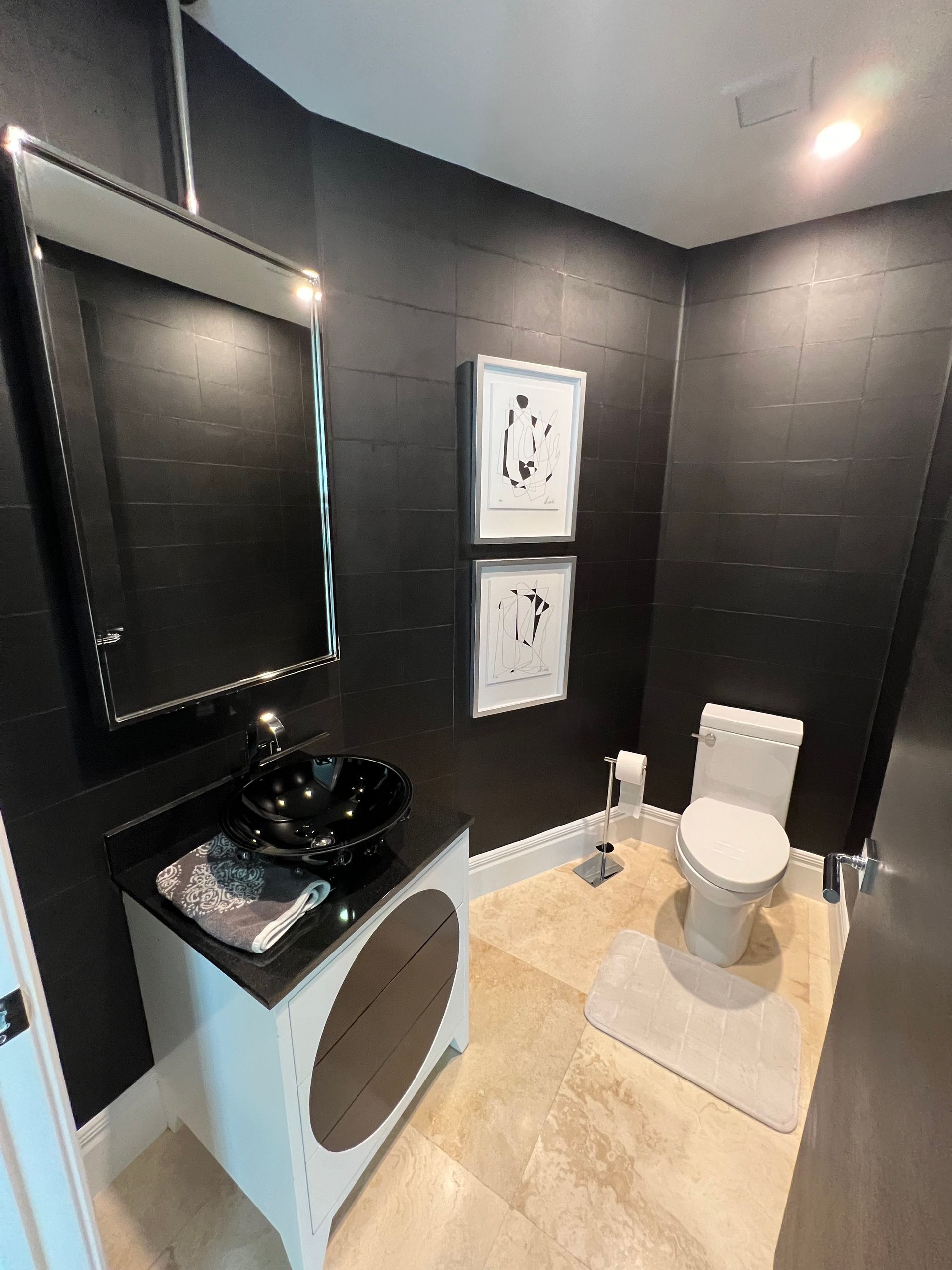 Black powder room with a vanity, toilet, and artwork; beige floor and white trim.