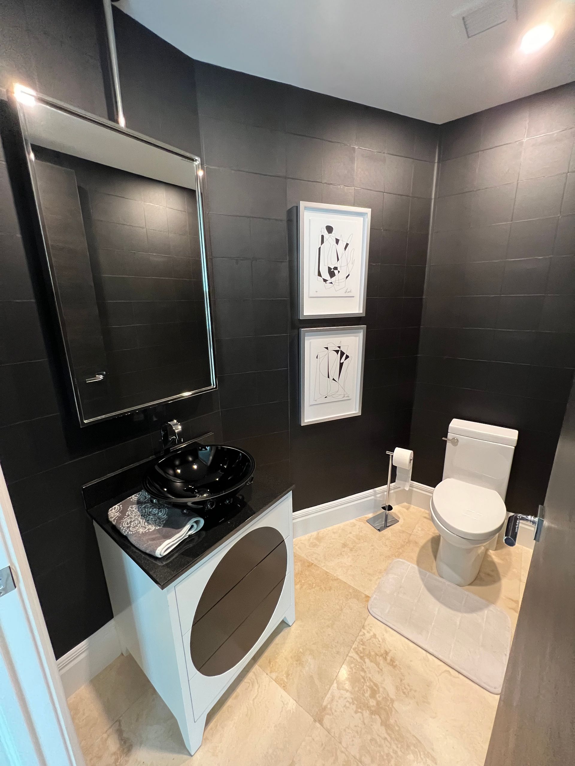 Black and white bathroom with dark walls, a black sink, white toilet, and beige floor.
