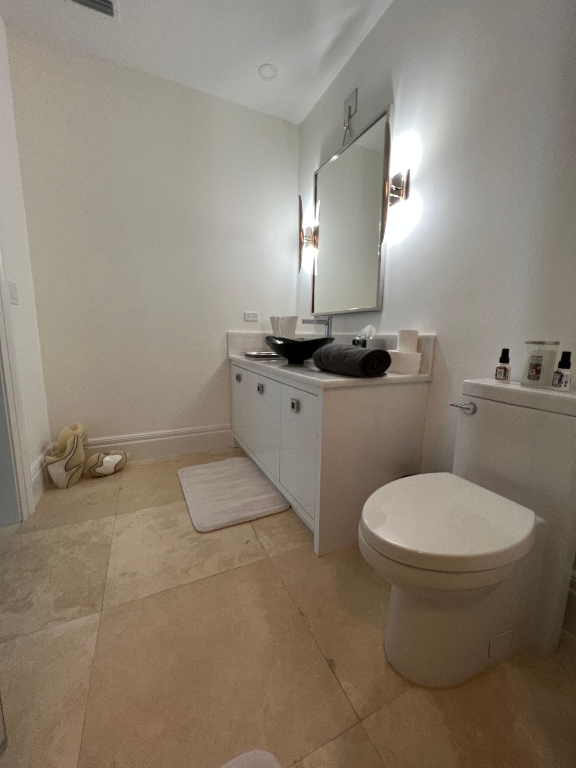 White bathroom with vanity, toilet, and beige tile floor.
