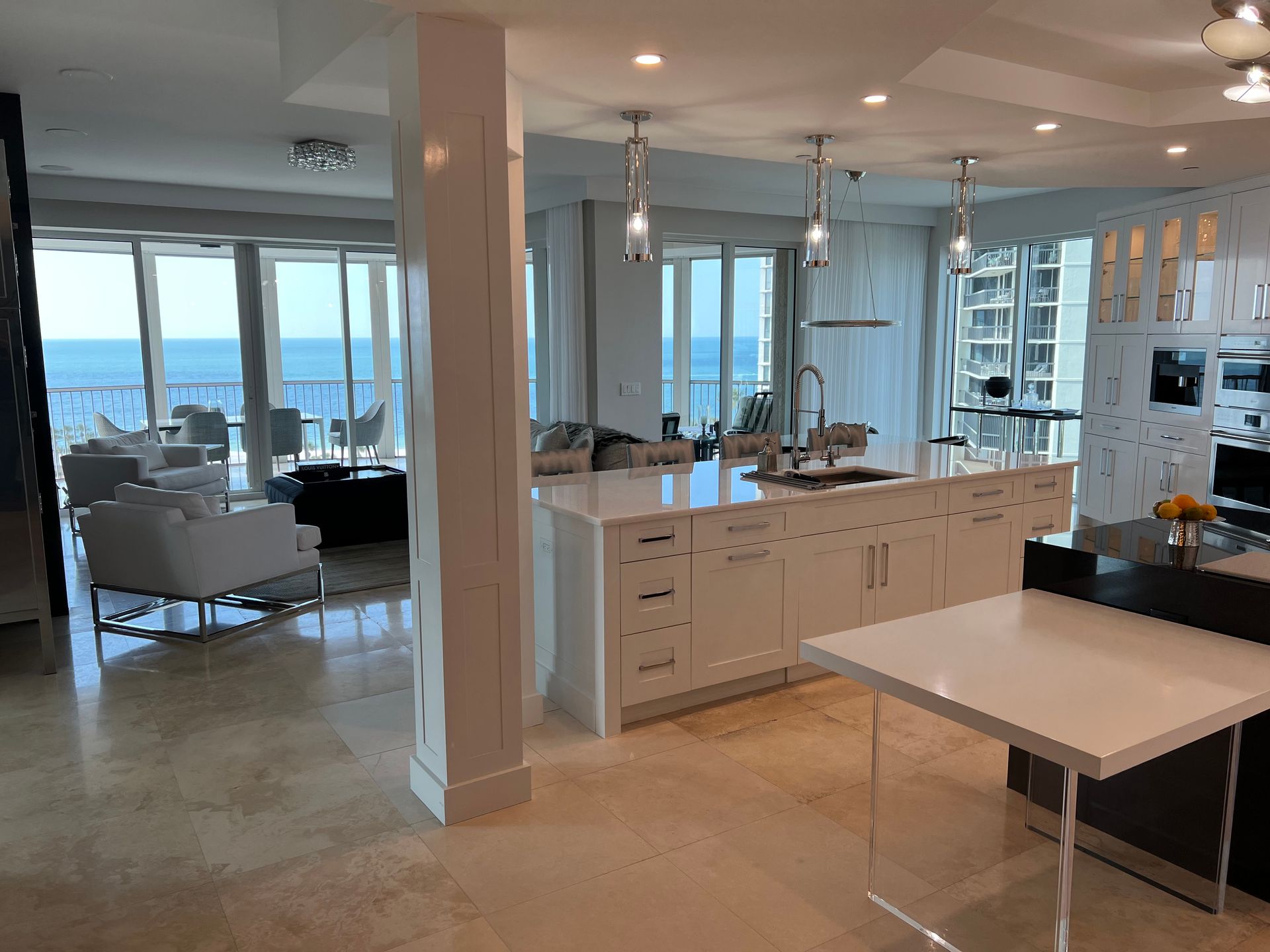 Modern kitchen with white cabinets, island, and ocean view through large windows.