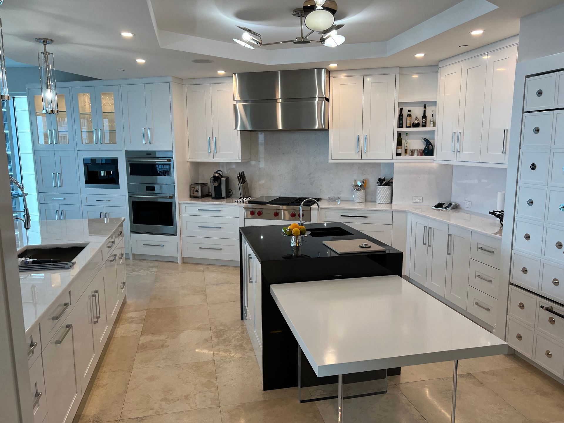 Modern white kitchen with black island, stainless steel appliances, and a white countertop.