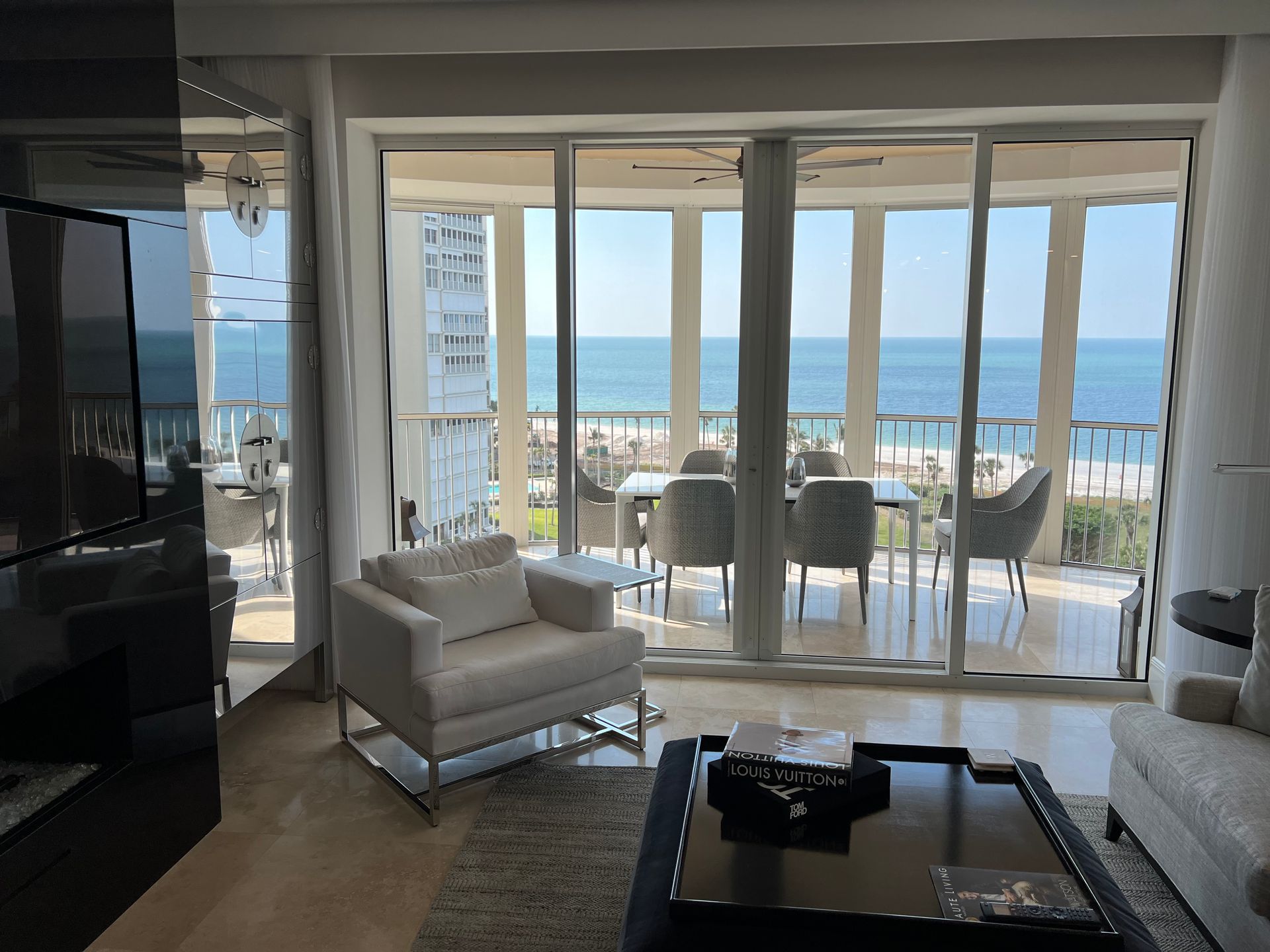 Living room with ocean view. White chair, black coffee table, and outdoor dining set.