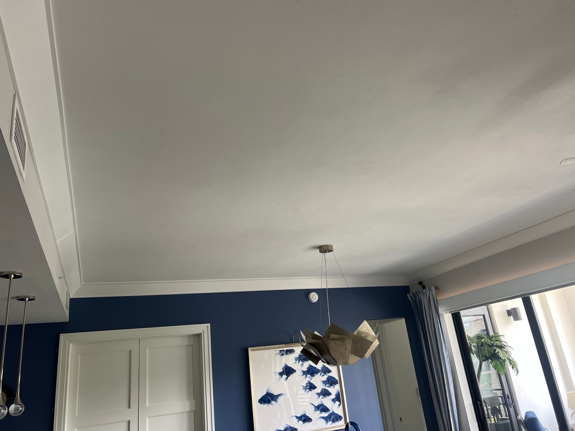 White ceiling with crown molding, above blue wall with art, windows, and a pendant light.