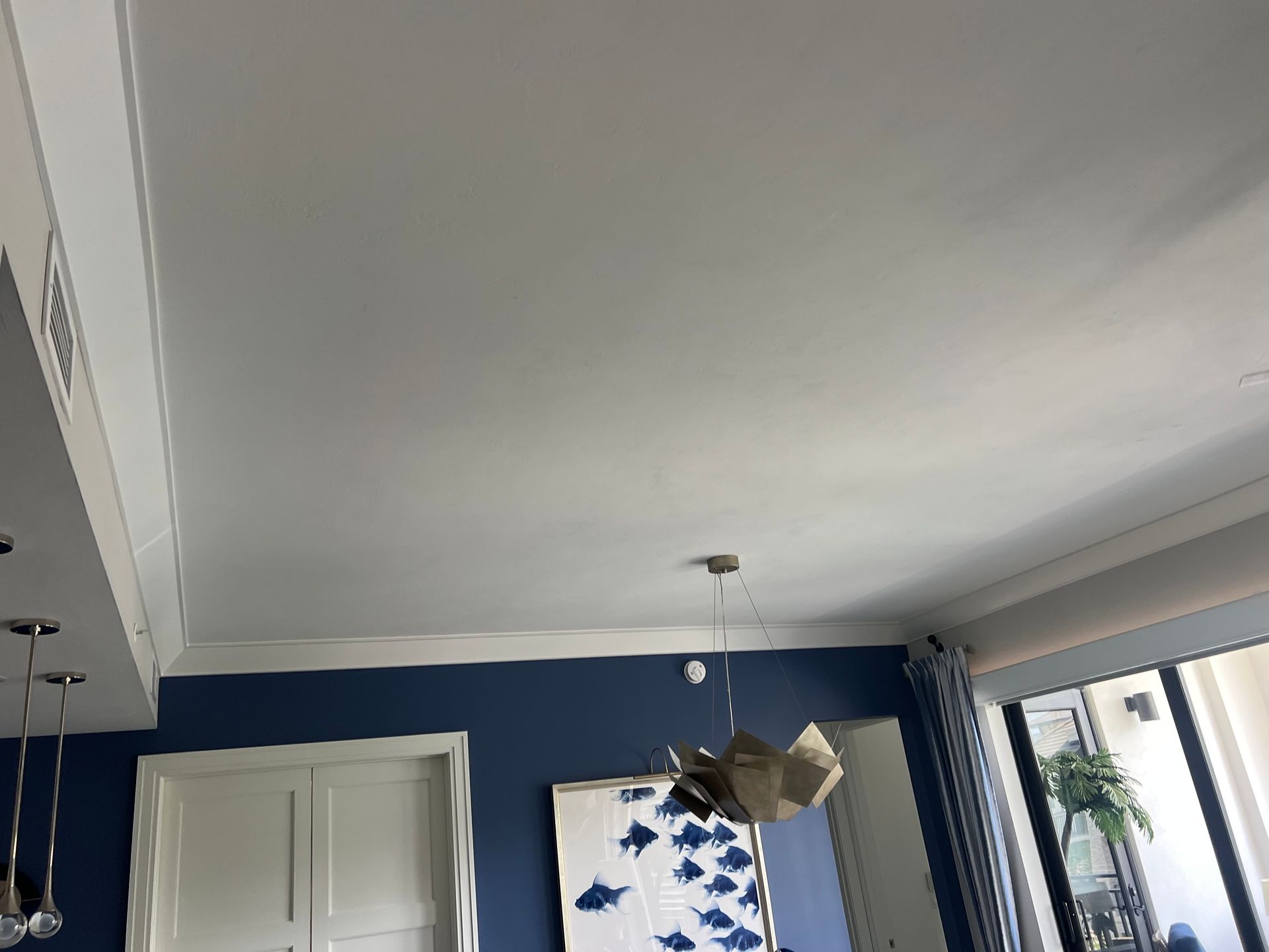 A ceiling with crown molding, a hanging lamp, a blue wall with art, and a window with blinds.