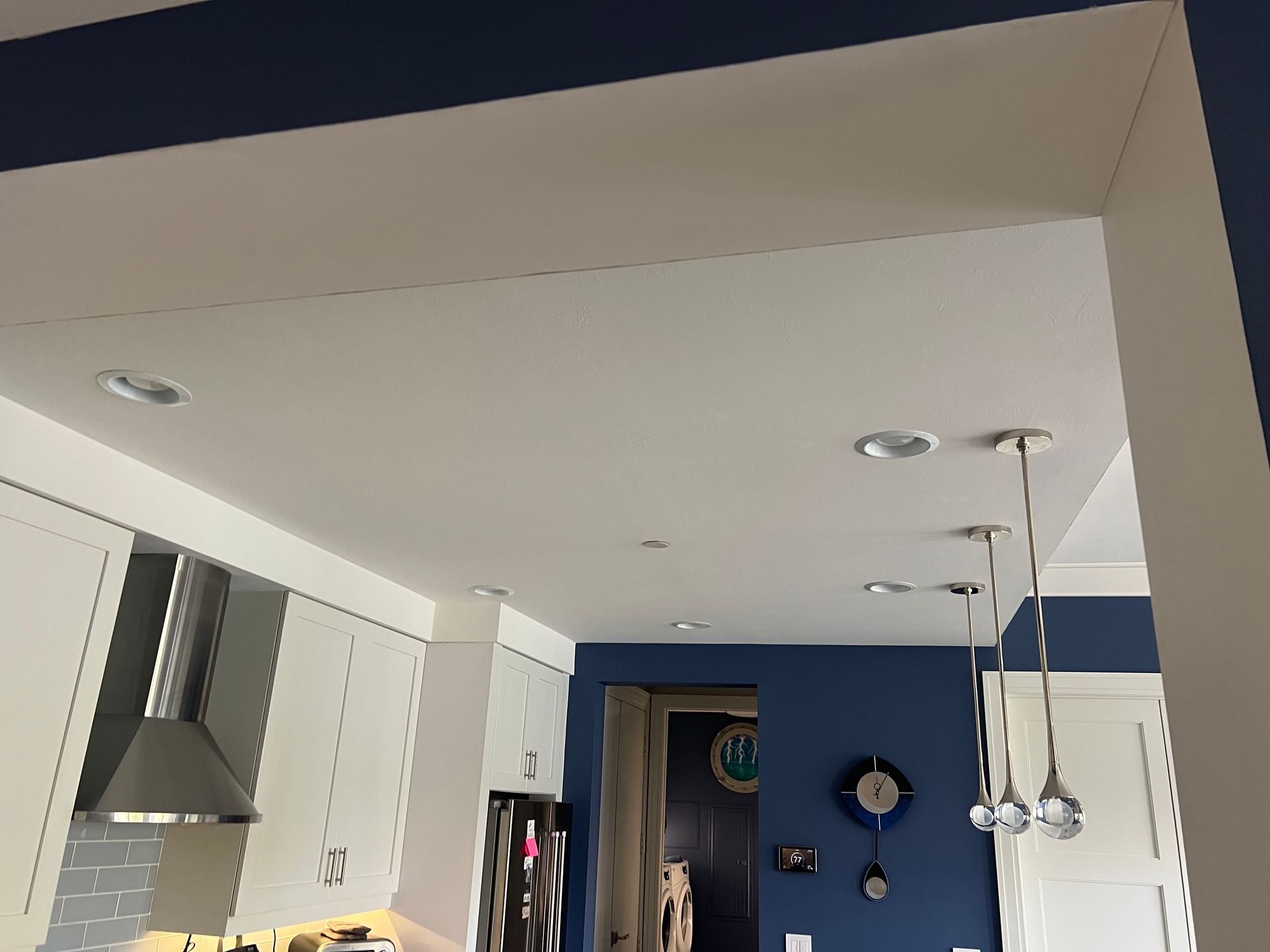 Kitchen ceiling with recessed lights, white cabinets, blue wall.