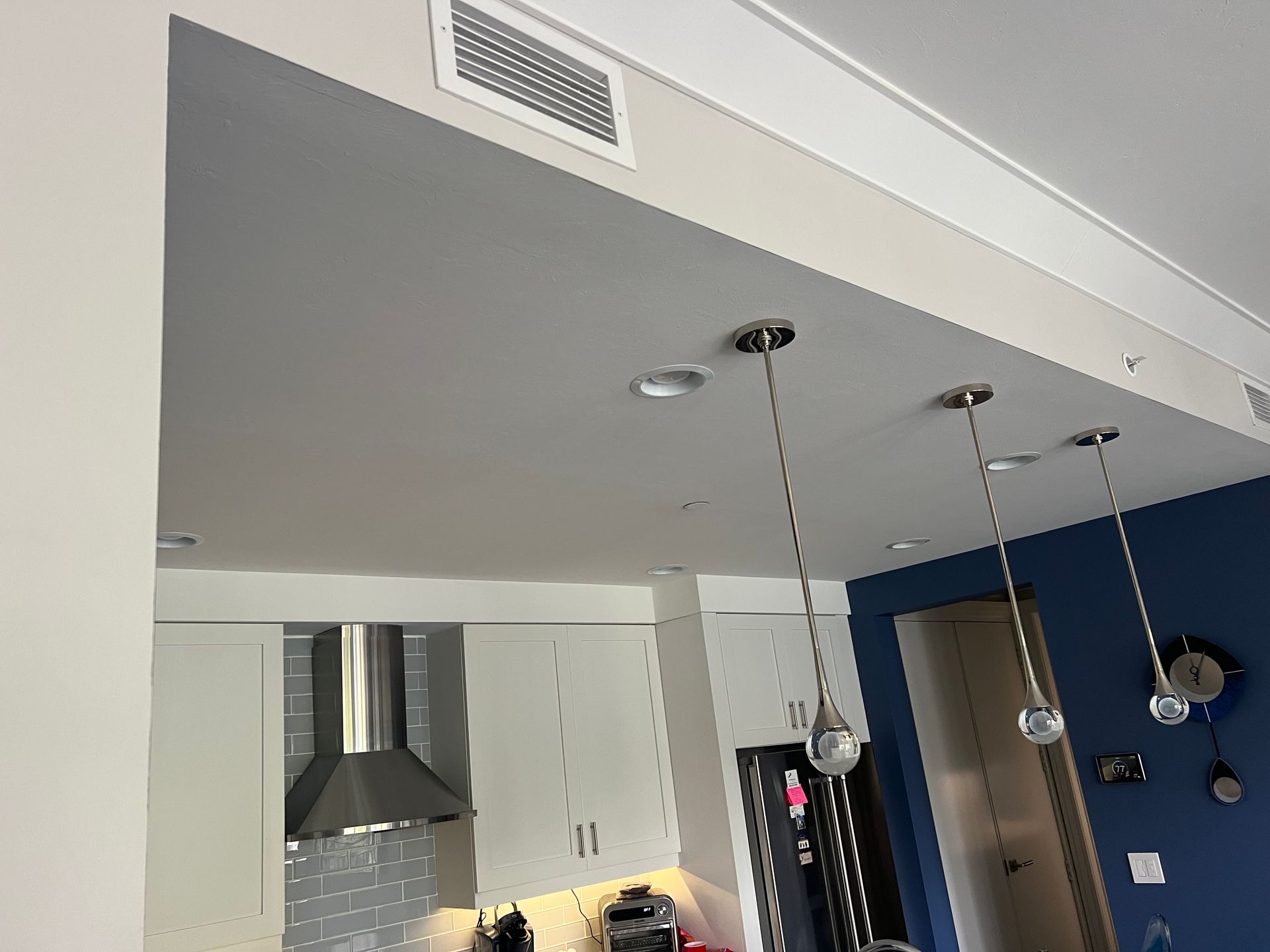 Kitchen with white cabinets, pendant lights, stainless steel hood, and dark blue wall.