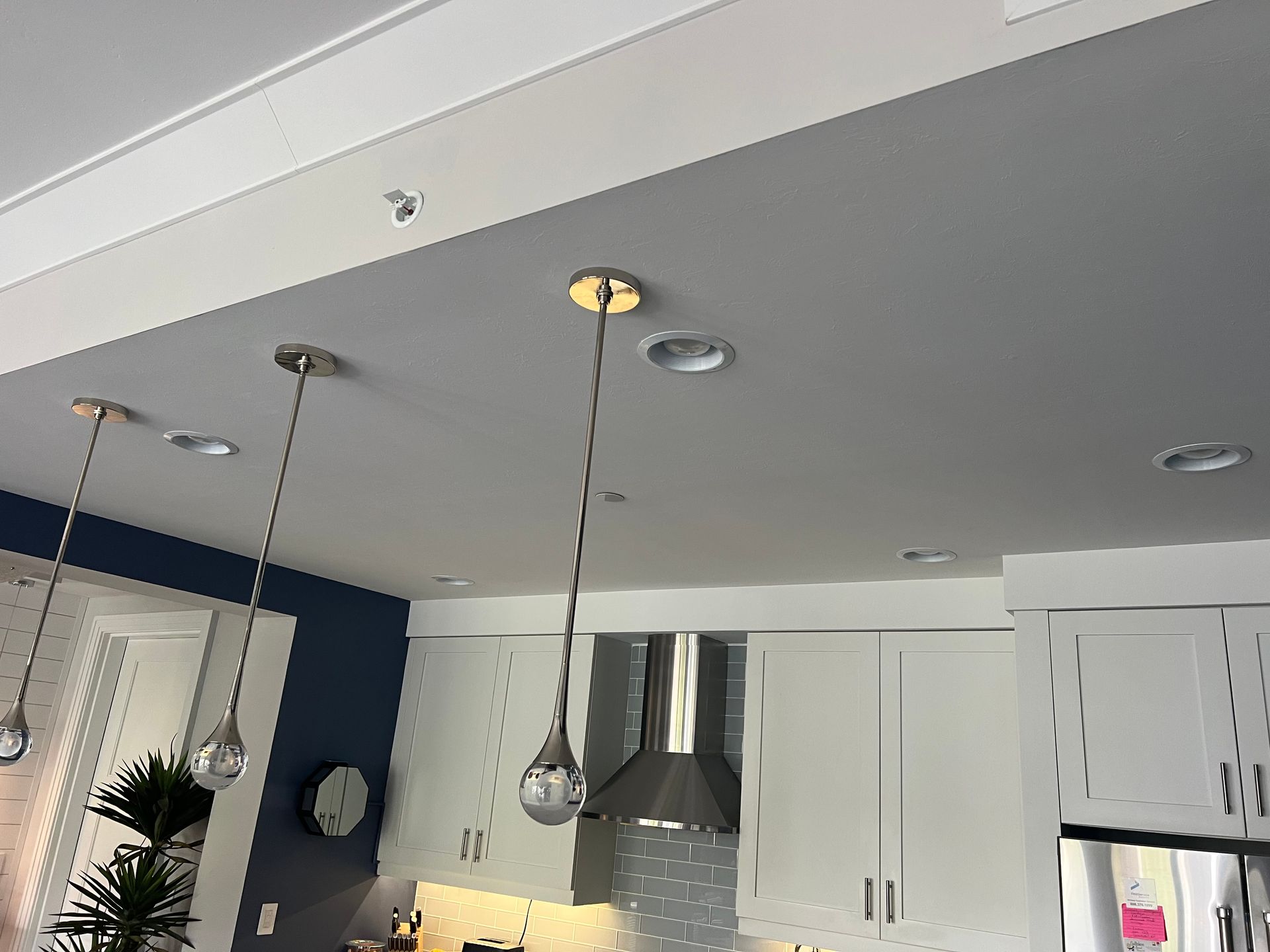 Ceiling with pendant lights over white cabinets, a range hood, and recessed lights.