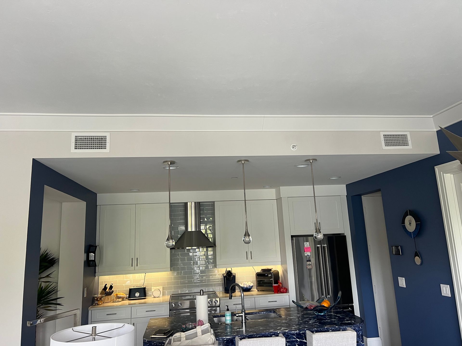 Kitchen with white cabinets, blue walls, island with pendant lights, and stainless steel appliances.
