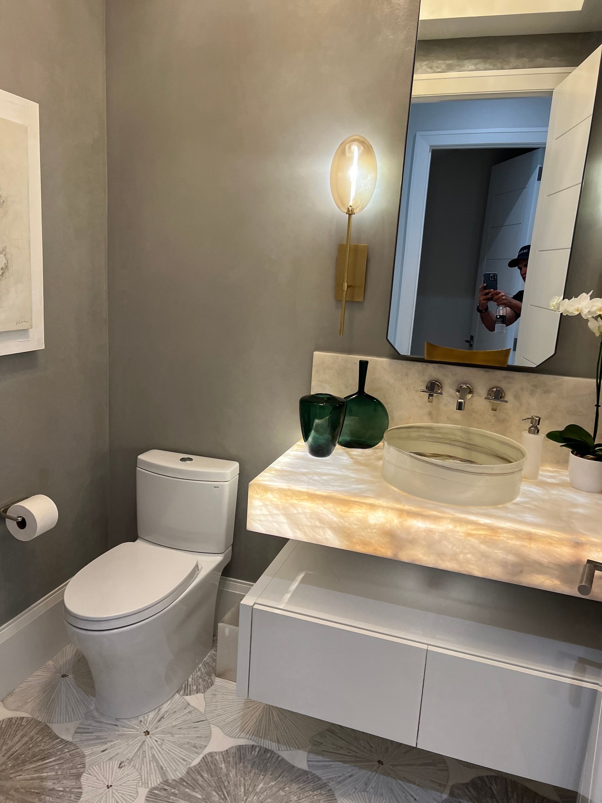 Modern bathroom with gray walls, white toilet, floating vanity, and unique patterned floor.