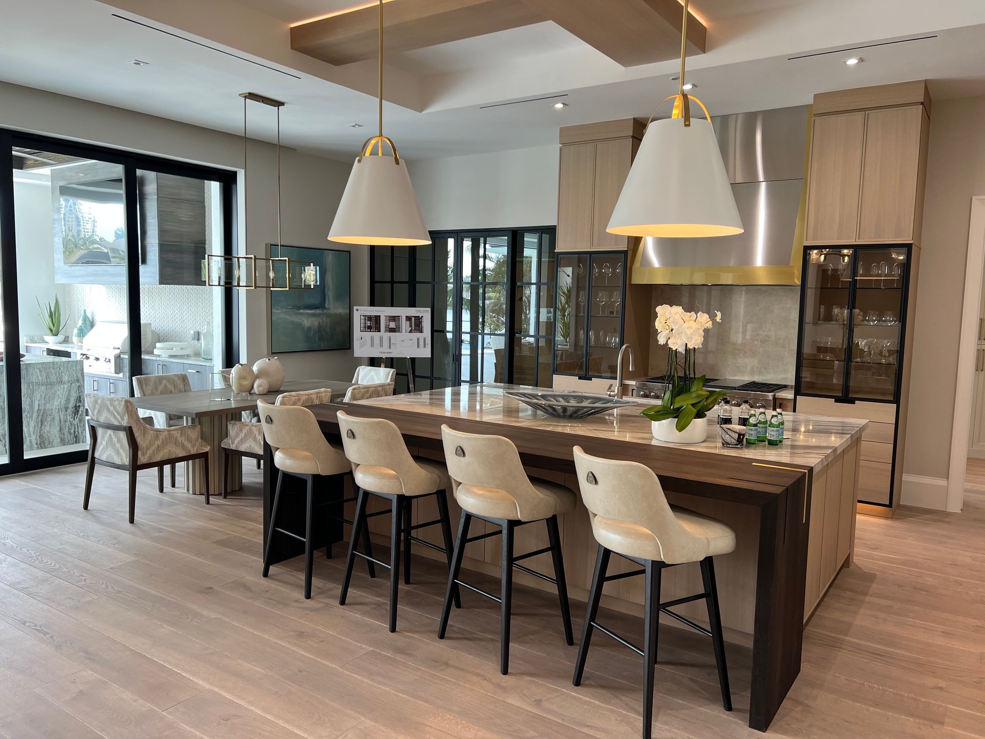 Modern kitchen with island, pendant lights, and bar stools. Light wood cabinets and flooring.