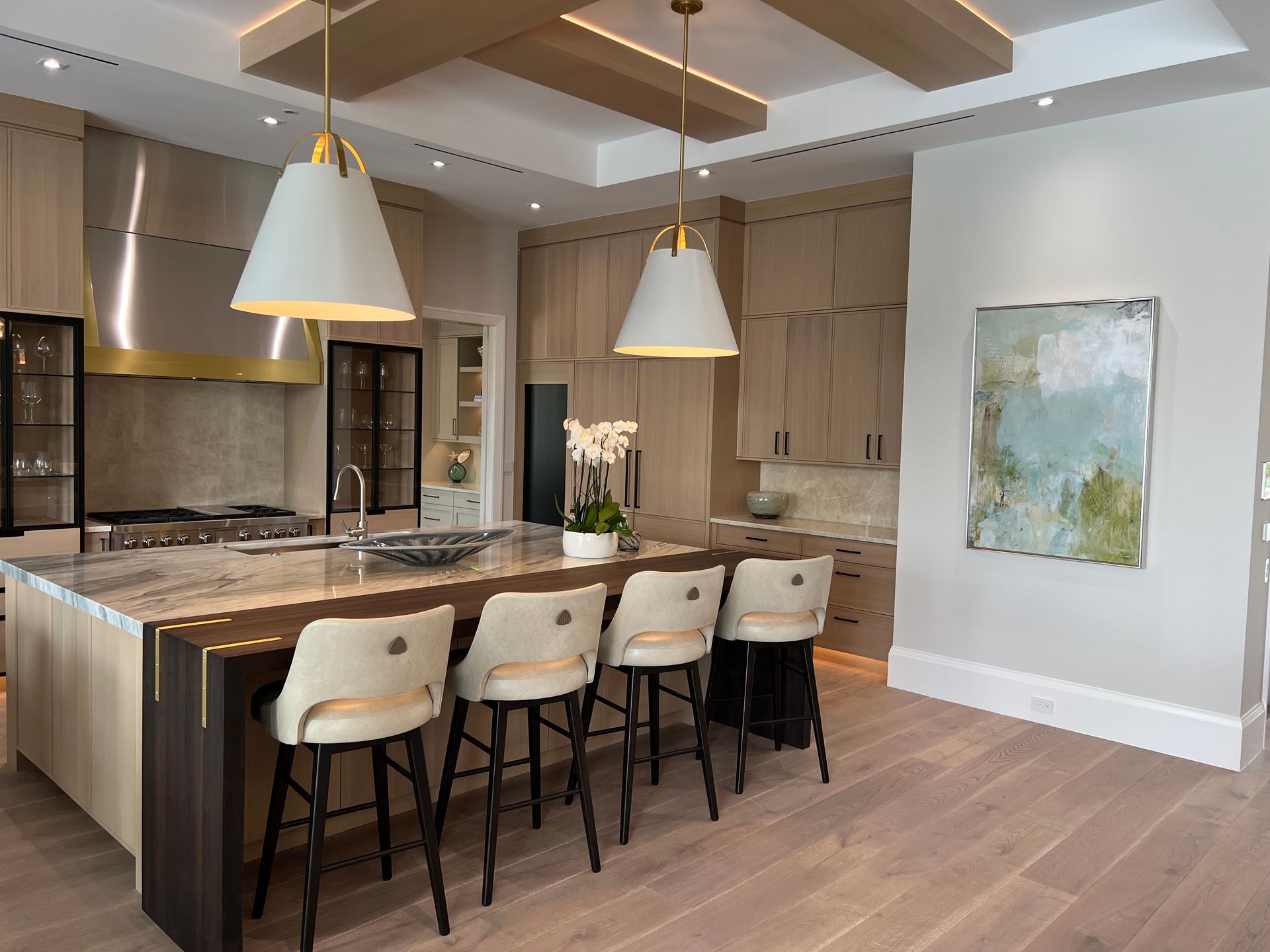 Modern kitchen with island seating, pendant lights, neutral tones, and artwork.