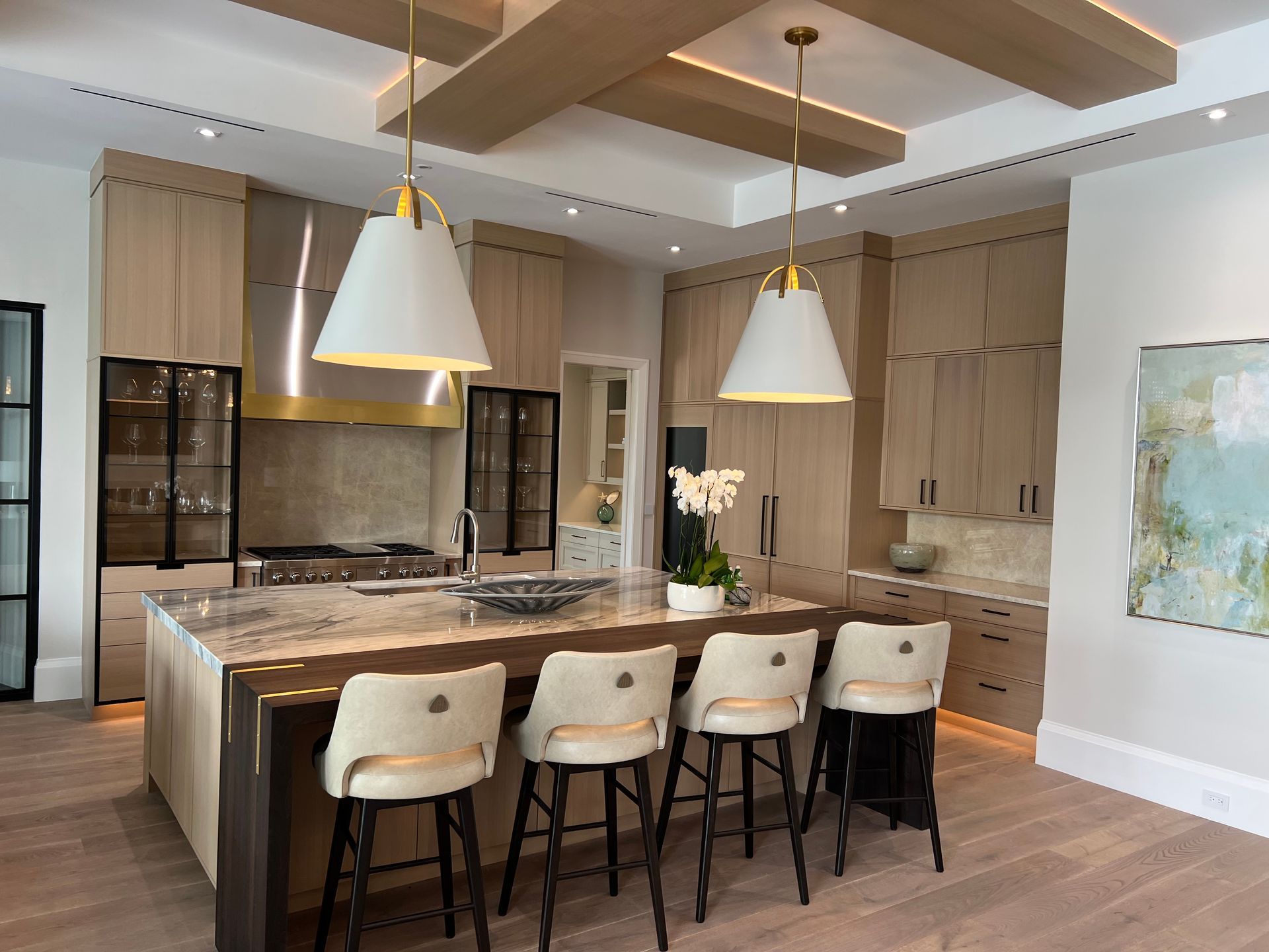 Modern kitchen with beige cabinets, island with bar stools, pendant lights, and hardwood floors.