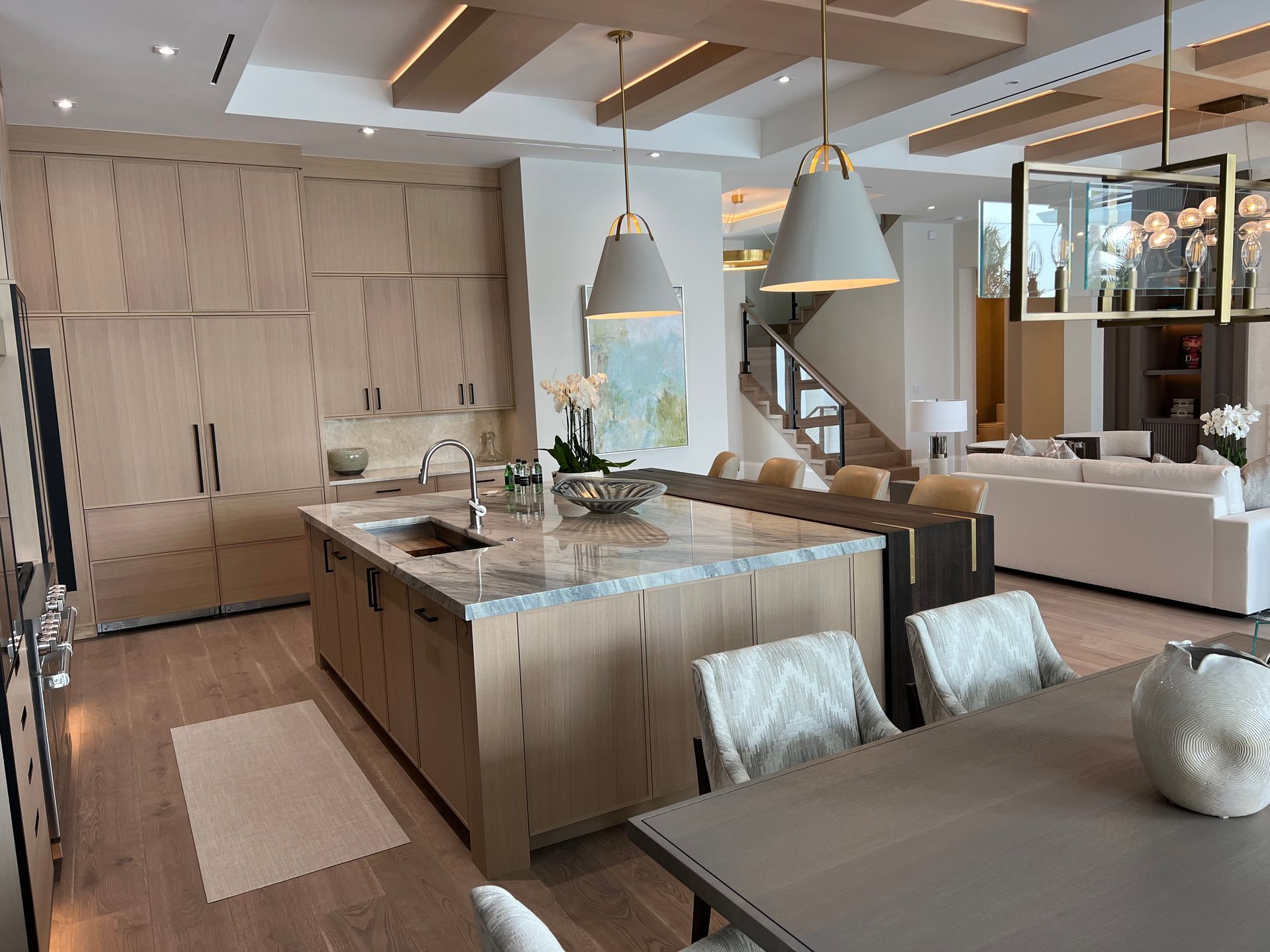 Modern kitchen with light wood cabinetry, island, dining table, and open to a living area.