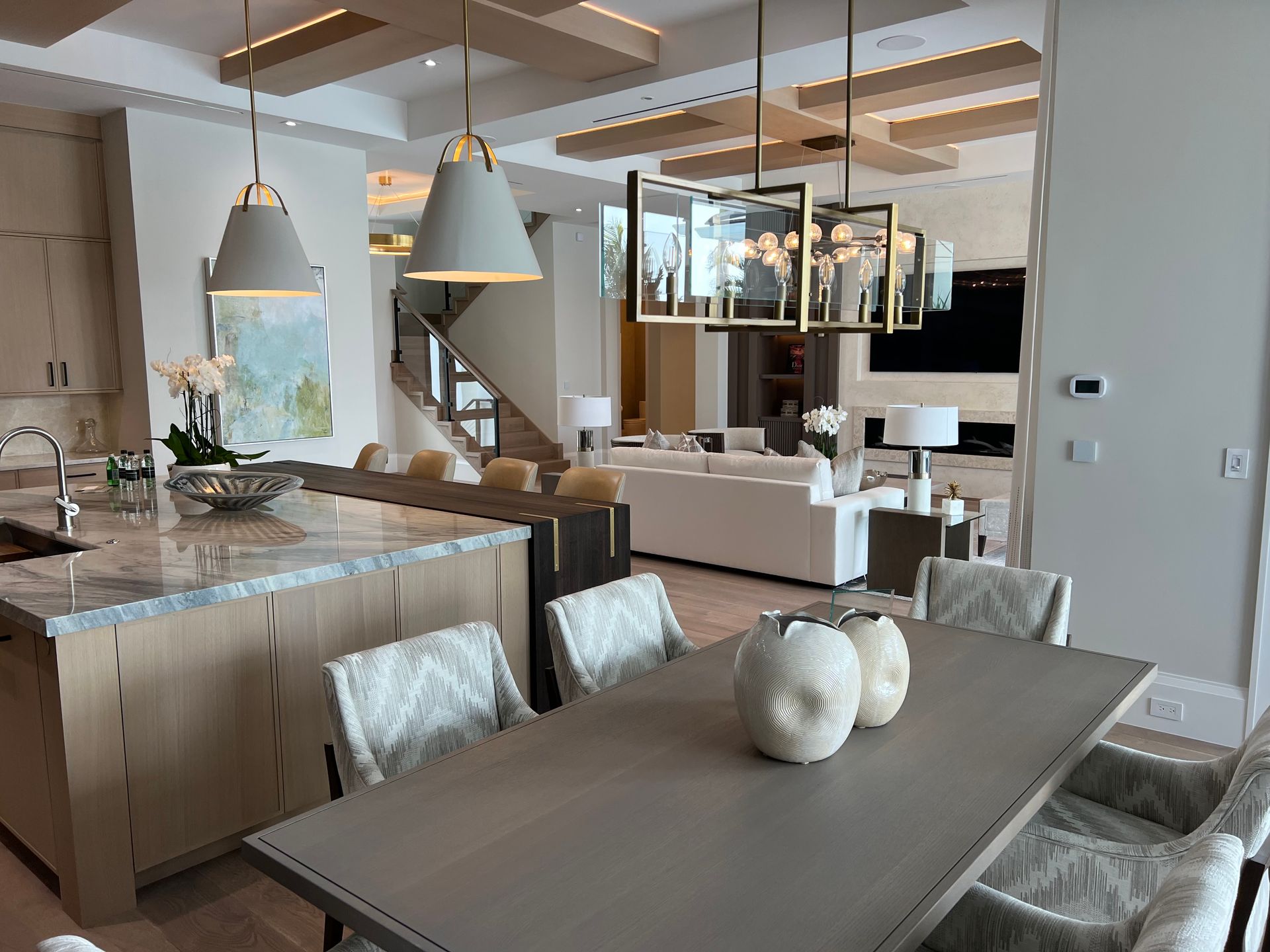 Open-concept kitchen and living room. Features include a dining table, island with pendant lights, and a staircase.