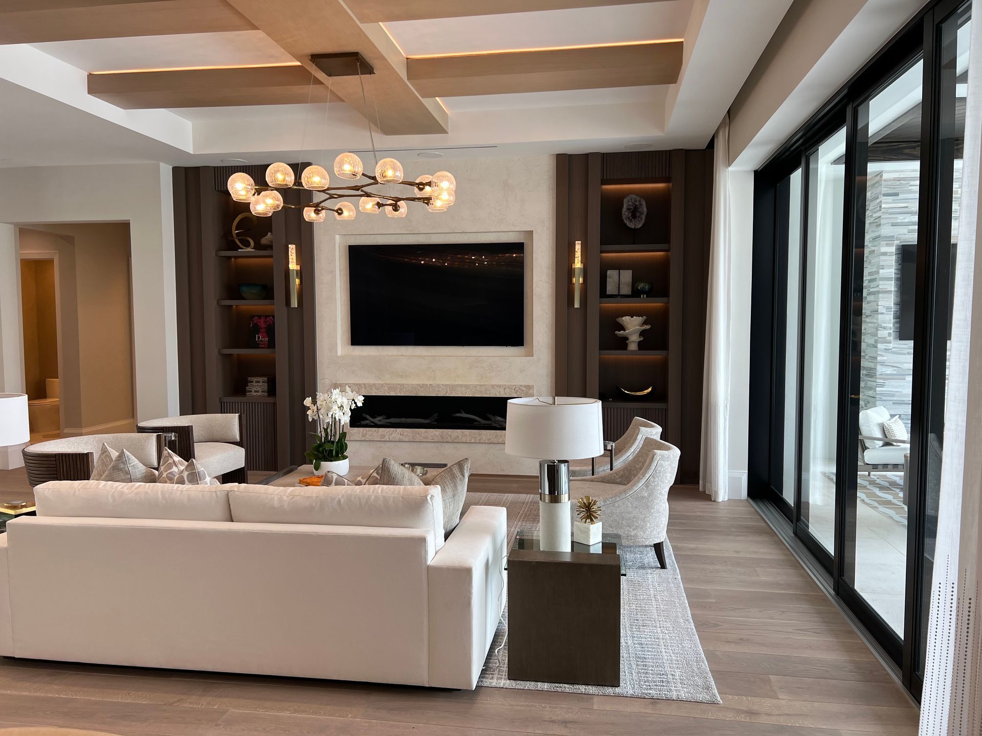 Living room with white sofa, built-in shelves, fireplace, large TV, and sliding glass doors.