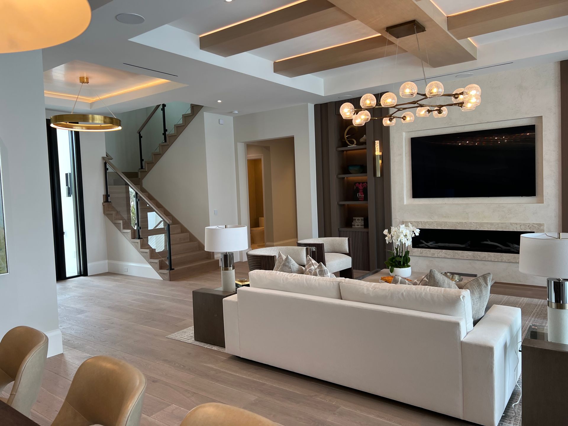 Modern living room with white sofa, fireplace, stairs, and chandelier.